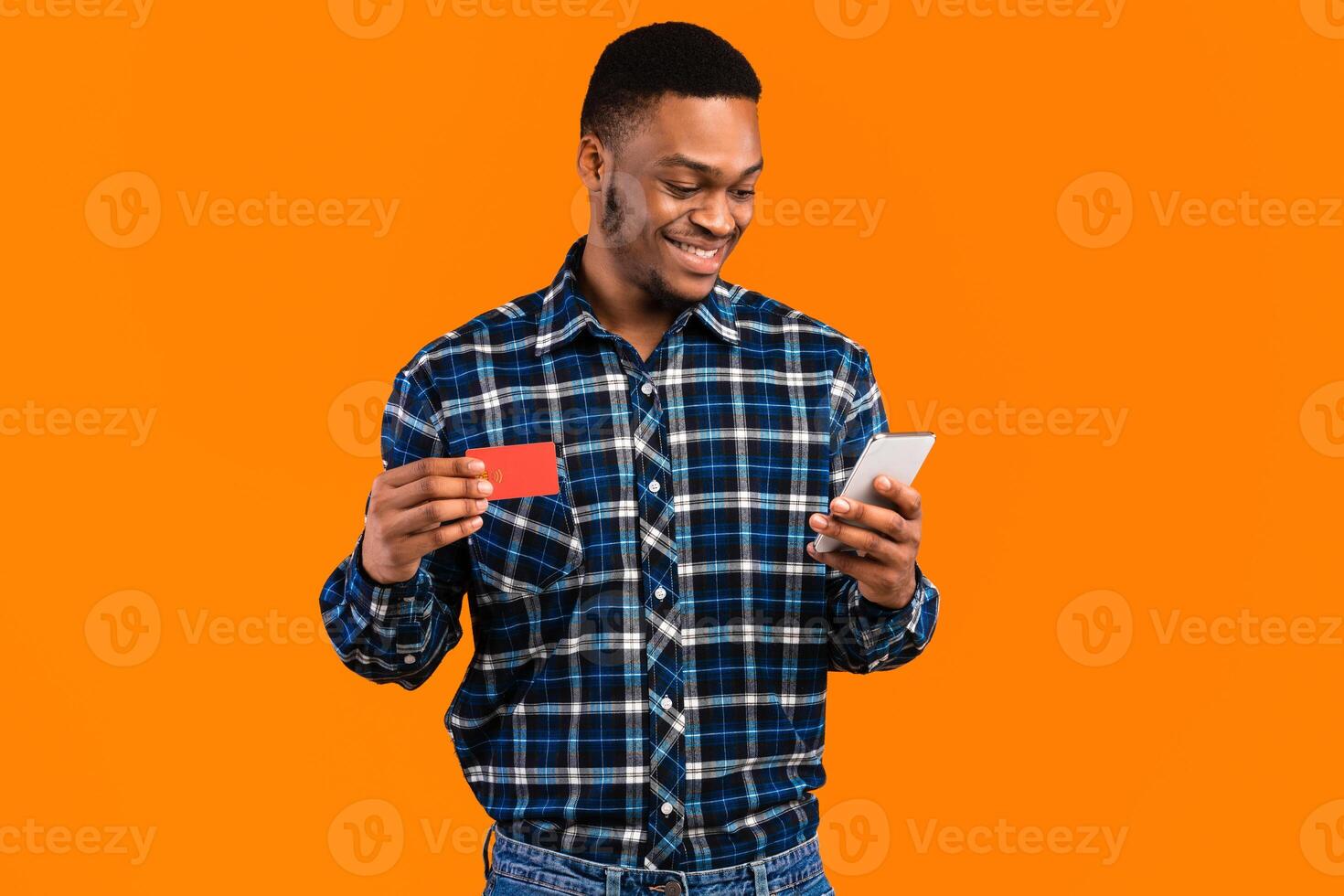 Mobile Banking. Happy Black Man Using Smartphone Holding Credit Card Shopping Online Standing On Yellow Background In Studio photo