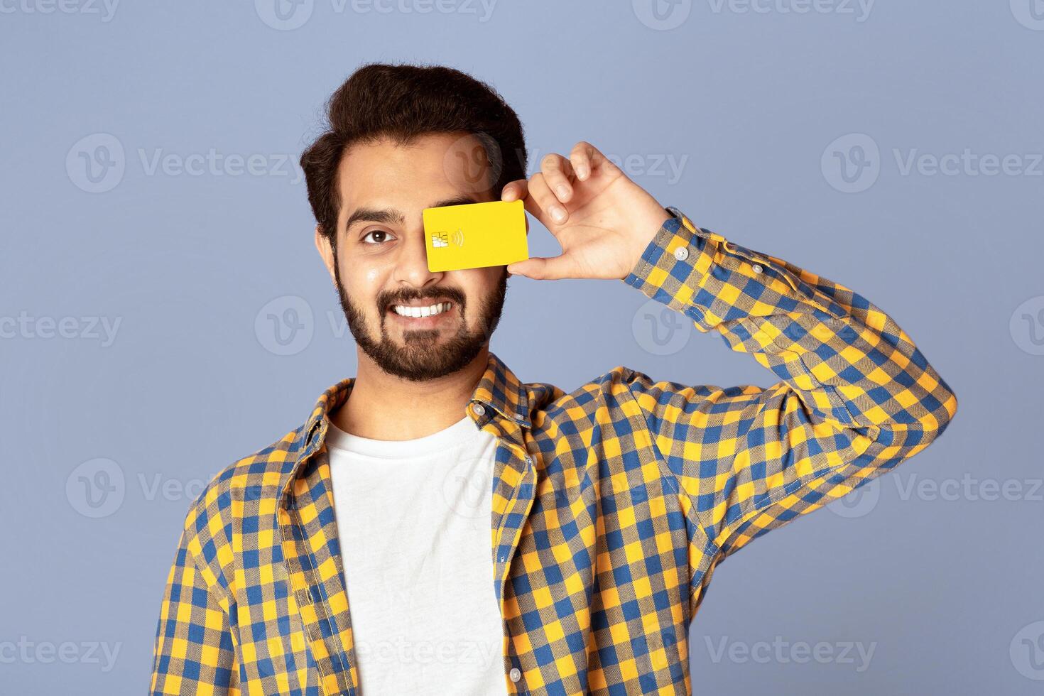 Positive Indian guy closing eye with contactless credit card over violet background photo