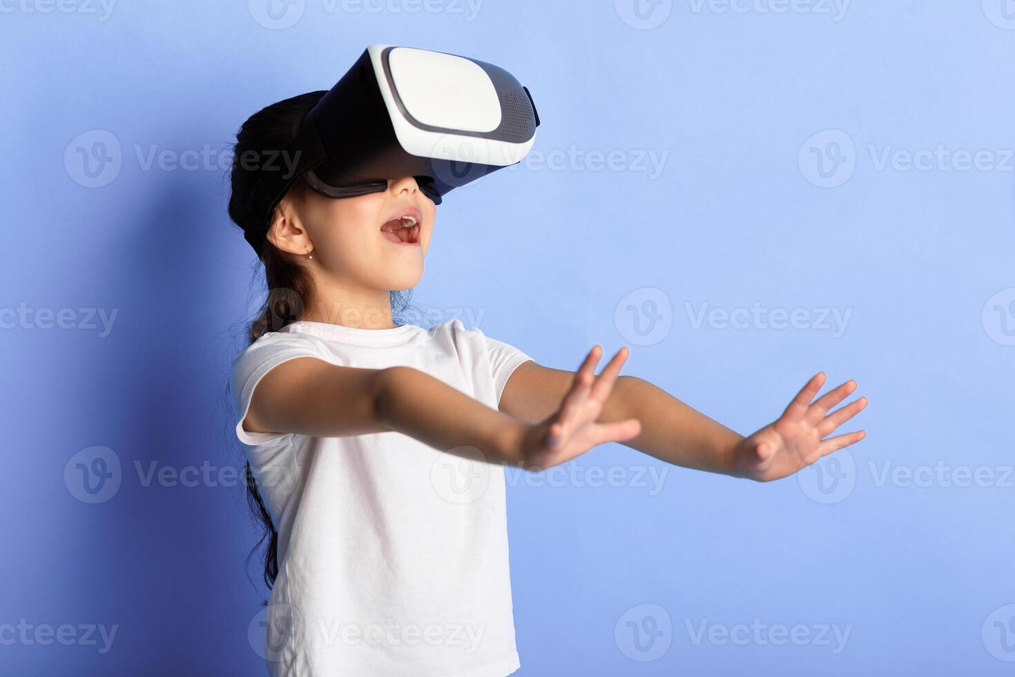 Digital Education And Entertainment. Portrait of excited asian child wearing VR headset and experiencing virtual reality, isolated over blue studio background. Girl Using Technology Of Future. photo