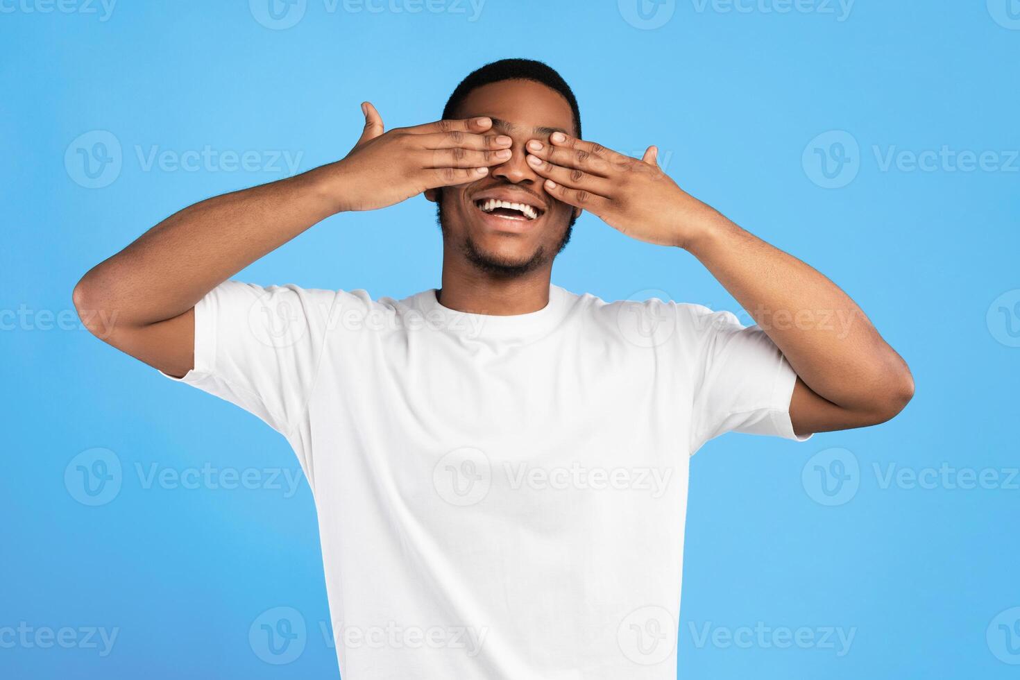 Cheerful African American Guy Covering Eyes With Hands Standing On Blue Background In Studio. I Don't Look Concept photo