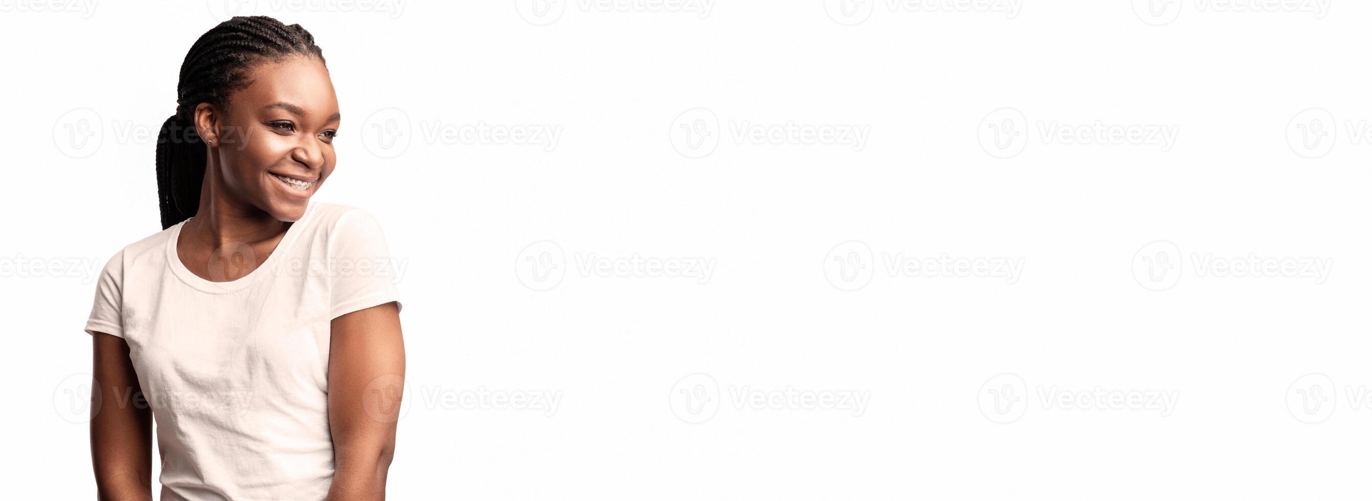 A young woman with braided hair and a bright smile poses confidently against a plain white background, showcasing her joyful demeanor and relaxed attitude. photo