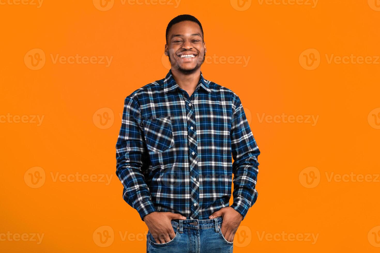 Black Millennial Guy Smiling To Camera Standing Holding Hands In Pockets Posing Over Yellow Background. Studio Shot photo
