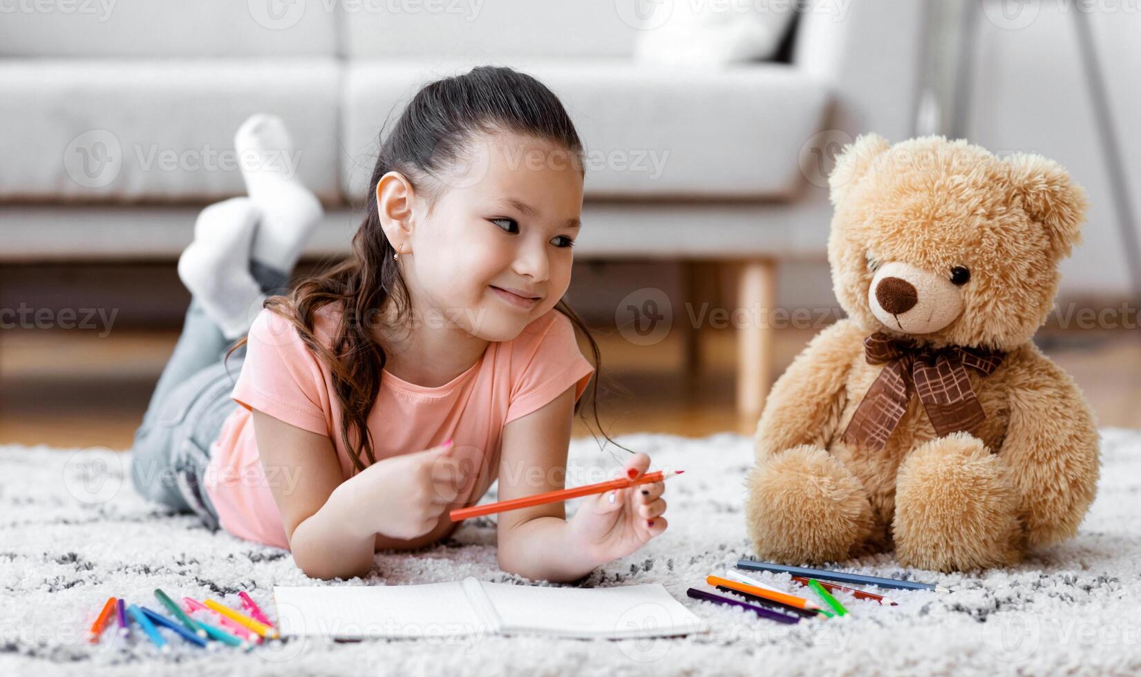 Kid's Leisure. Cute Korean Girl Drawing Playing With Bear Toy Lying On Floor At Home. Panorama photo