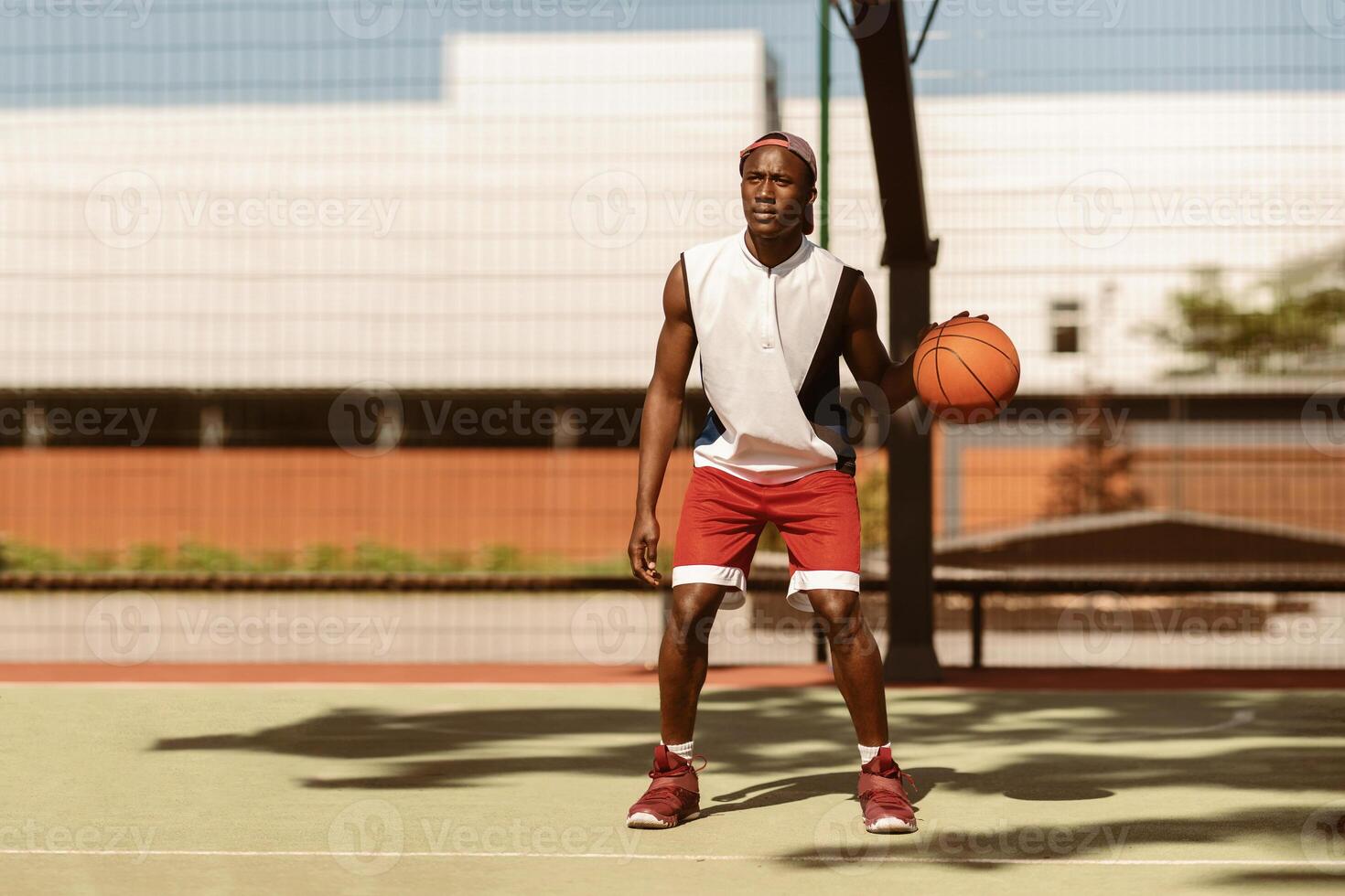 Serious black sportsman dribbling ball at basketball court outside photo