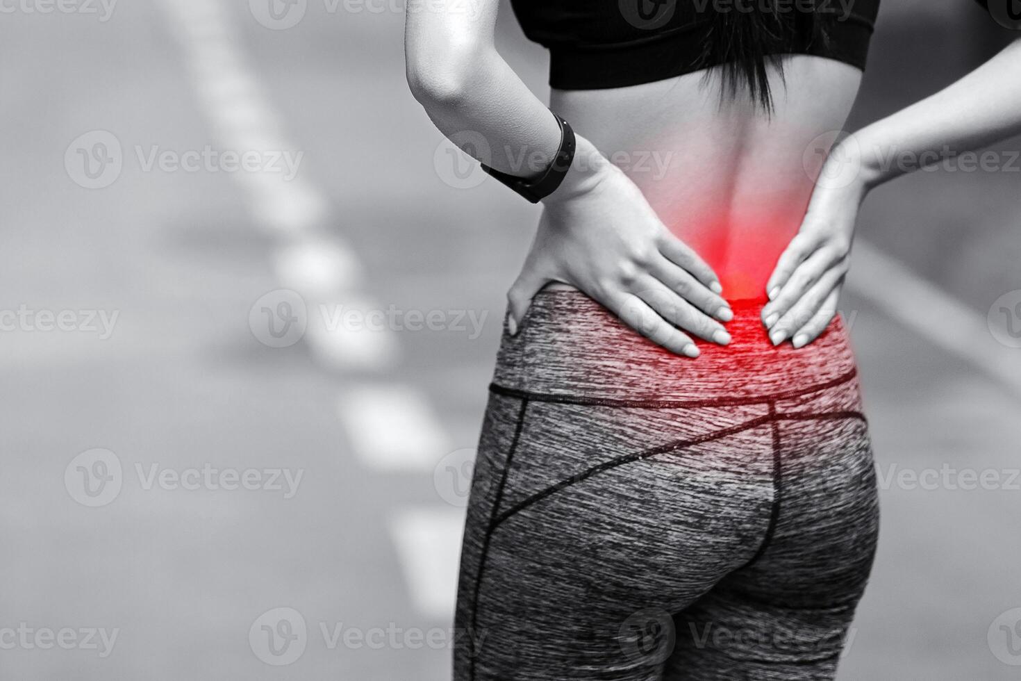 Lower Back Ache. Female athlete rubbing hurt back with painful injury, touching inflamed zone, black and white image with red sore spot, panorama photo