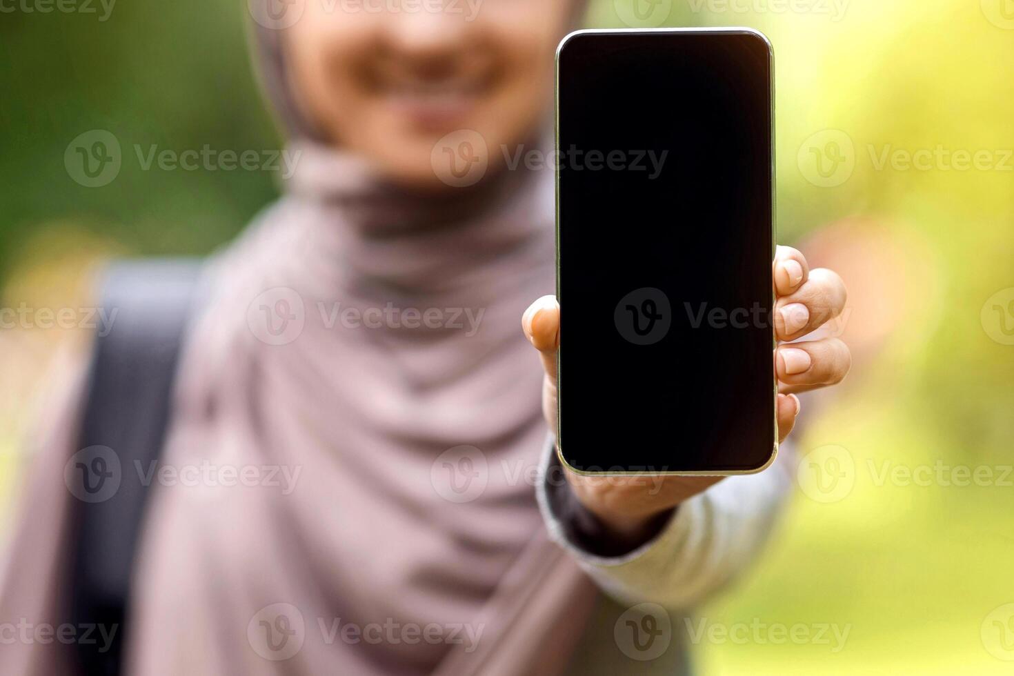 New mobile app. Muslim girl showing blank smartphone screen, park background, selective focus photo