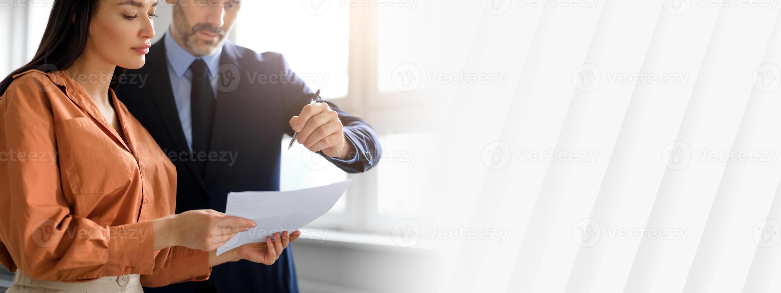 A businesswoman and businessman engage in a discussion while reviewing documents in a well-lit corporate office. They represent a partnership focused on achieving workplace success, copy space photo