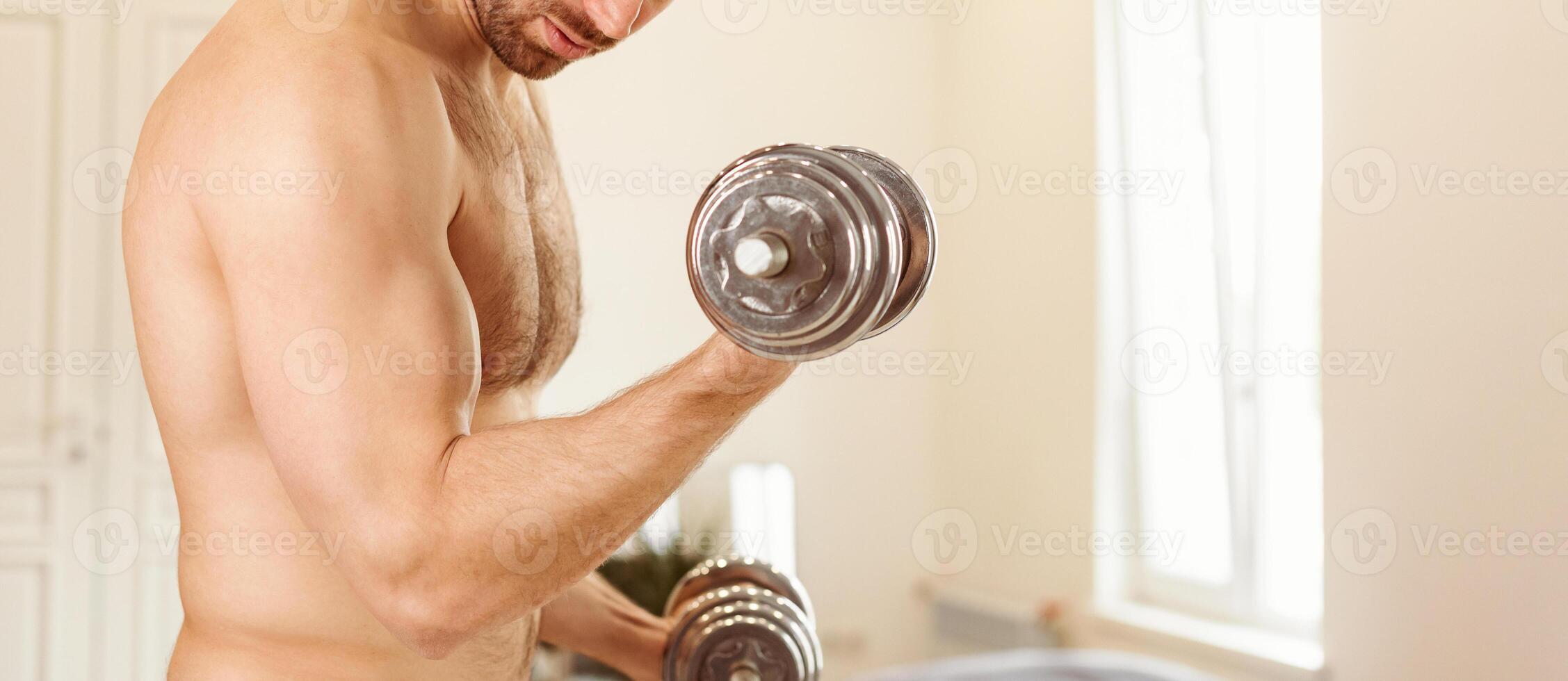 Unrecognizable Shirtless Muscular Man Exercising With Dumbbells Training Standing At Home, Pumping Biceps Muscles. Domestic Male Workout With Dumbbell. Sporty Lifestyle. Cropped, Panorama, Free Space photo