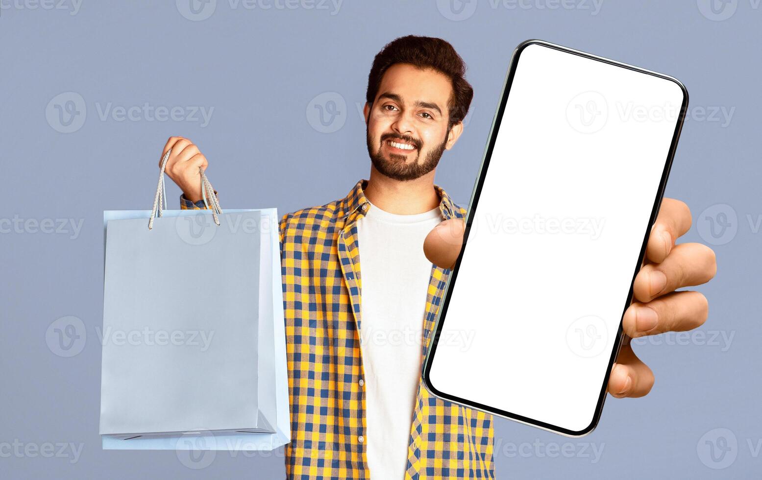 Smiling Indian man holding shopping bags and credit card on violet background, panorama photo