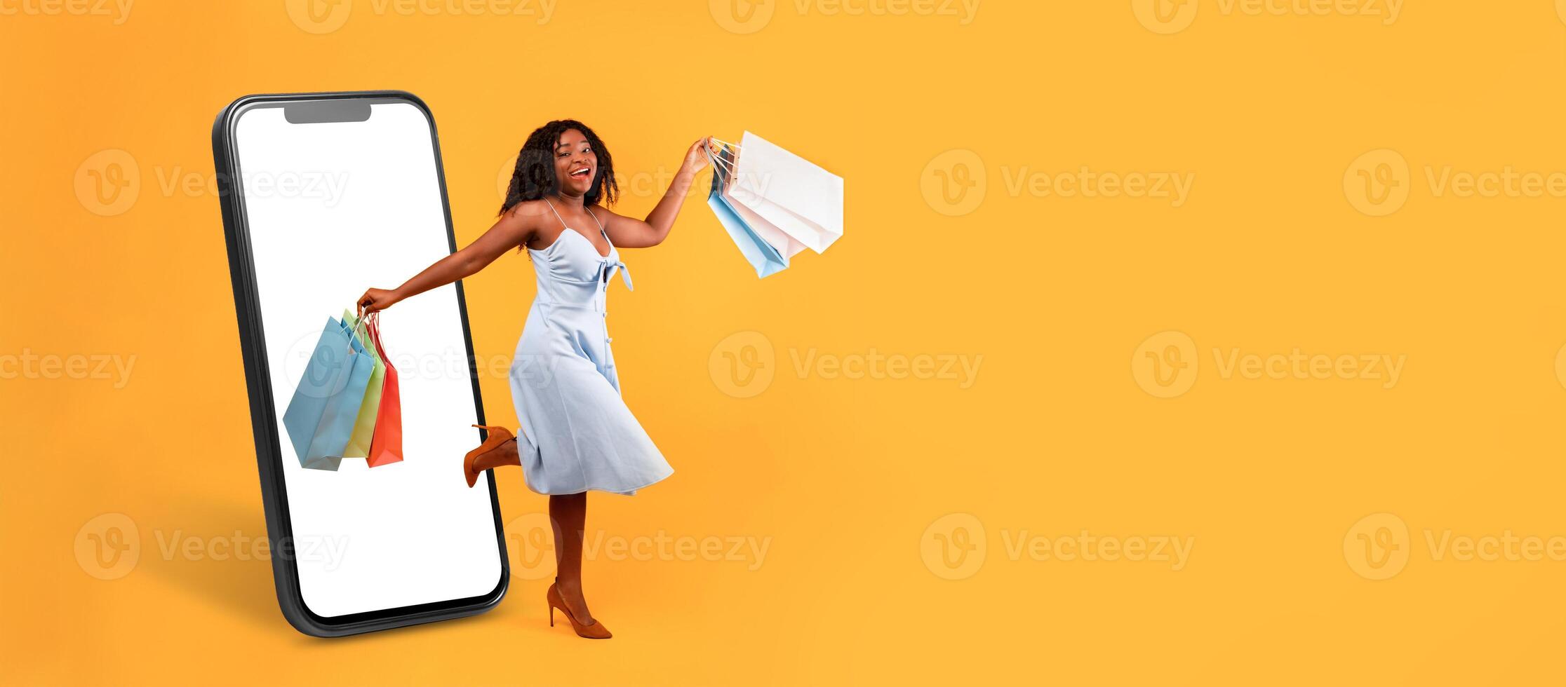 A shopper joyfully holds colorful shopping bags while interacting with their smartphone. The large device displays a web store interface against a vibrant yellow background. photo