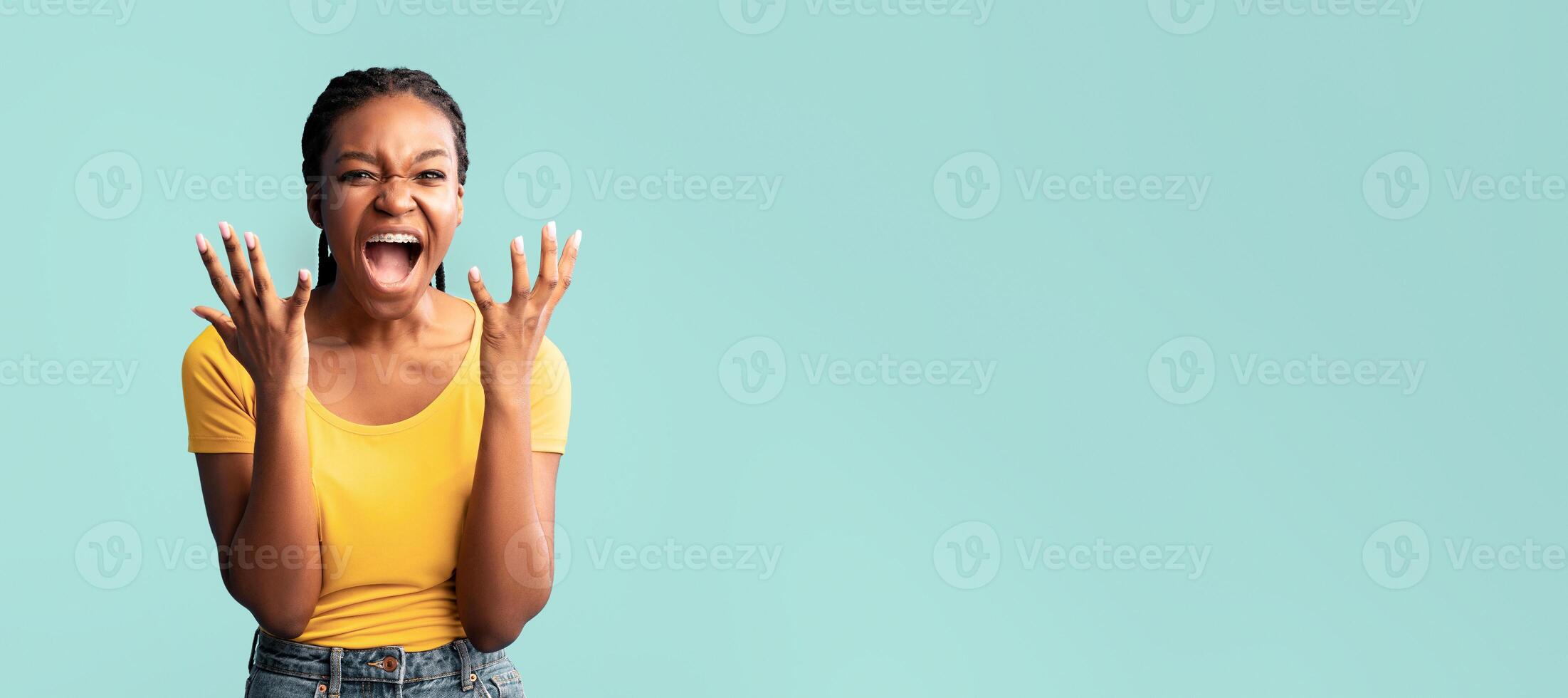 A woman in a yellow shirt smiles widely, raising her hands in delight. She showcases her enthusiasm and carefree spirit against a bright blue backdrop, creating a vibrant atmosphere. photo