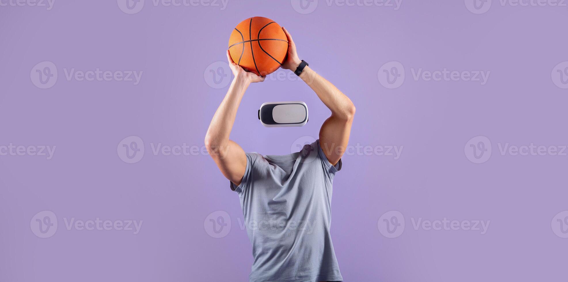 A person wearing a virtual reality headset is jumping to shoot a basketball, with their head absent. The background is a vibrant purple, emphasizing the action and technology. photo