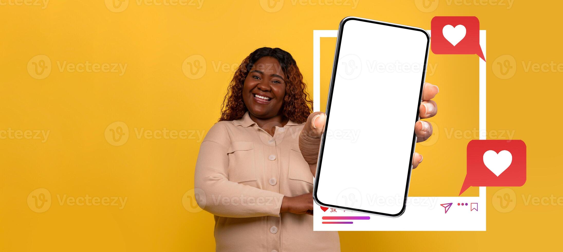 A smiling influencer holds a blank smartphone prominently displaying social media engagement icons. The vibrant yellow background enhances the lively atmosphere, ideal for online chats and messaging. photo
