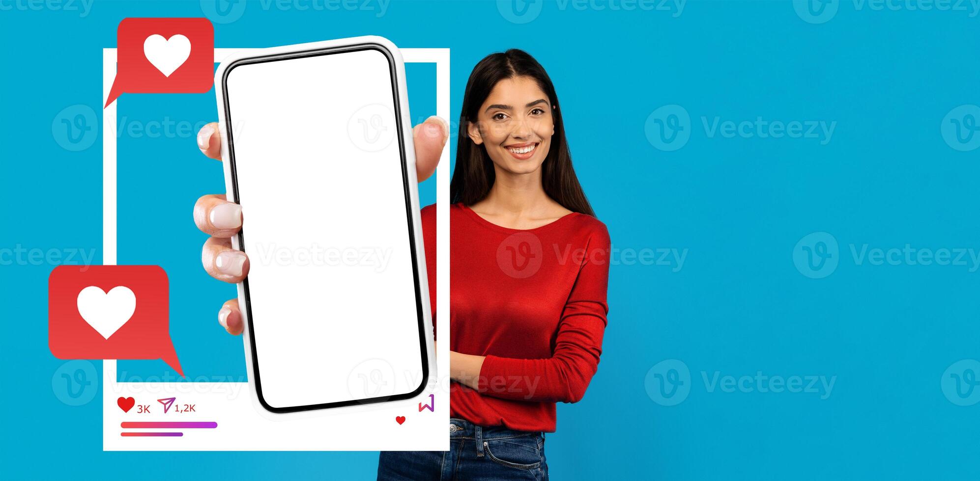 An influencer interacts with her smartphone against a vibrant blue backdrop, highlighting a blank screen for social media use. She presents chatting features depicted with hearts and comments. photo