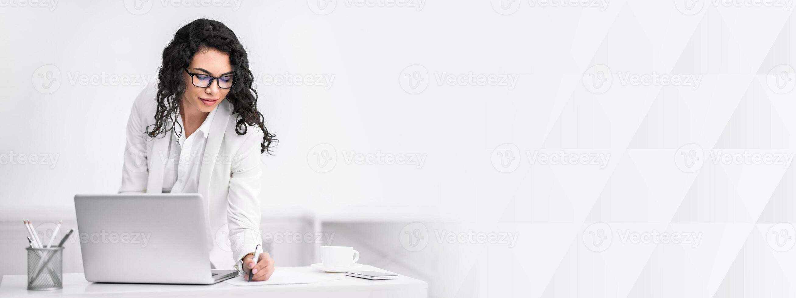 Note Taking. Happy mexican businesswoman in glasses at work, standing at desk and writing to do list, copy space photo