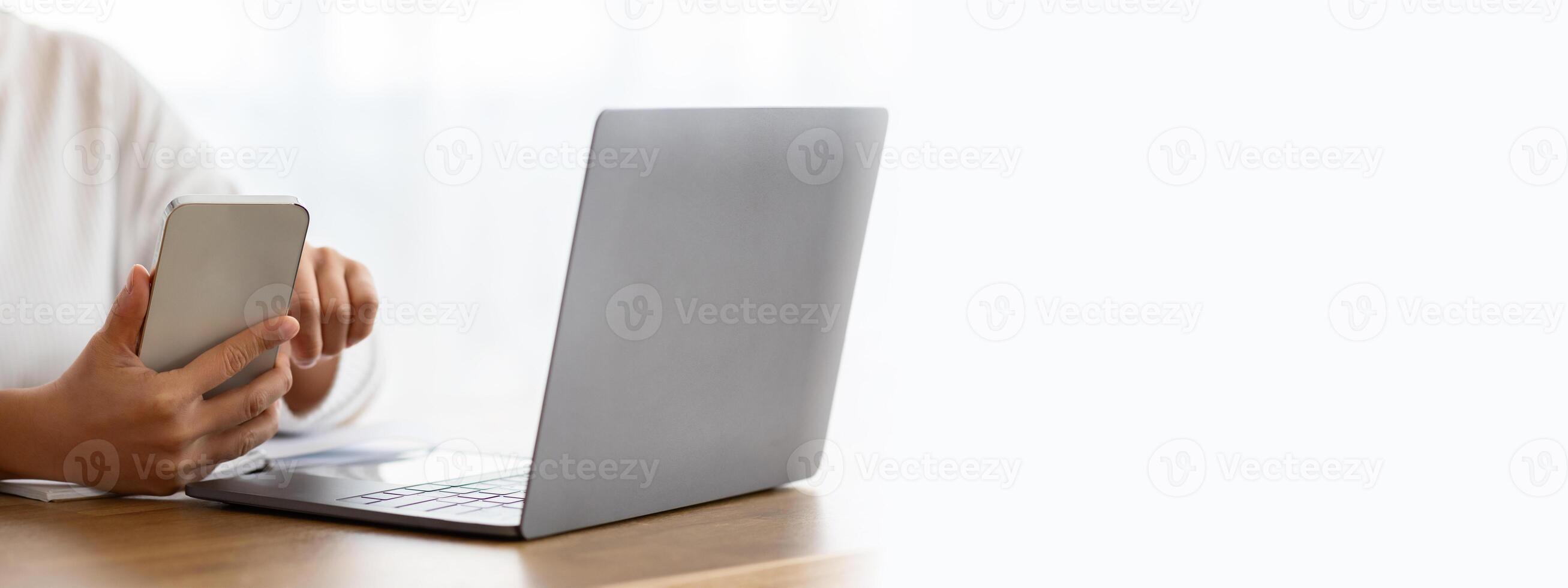 Cropped of woman entrepreneur working from home, multitasking, sitting at desk, using laptop computer and smartphone, answer emails, checking business app, web-banner photo