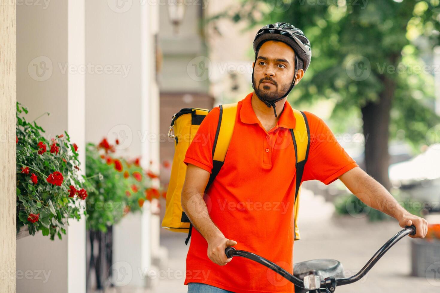 Eco transport and active lifestyle, mobile work in city. Serious millennial indian male courier in uniform and safety helmet, with big backpack and bicycle looking for clients address for delivery photo