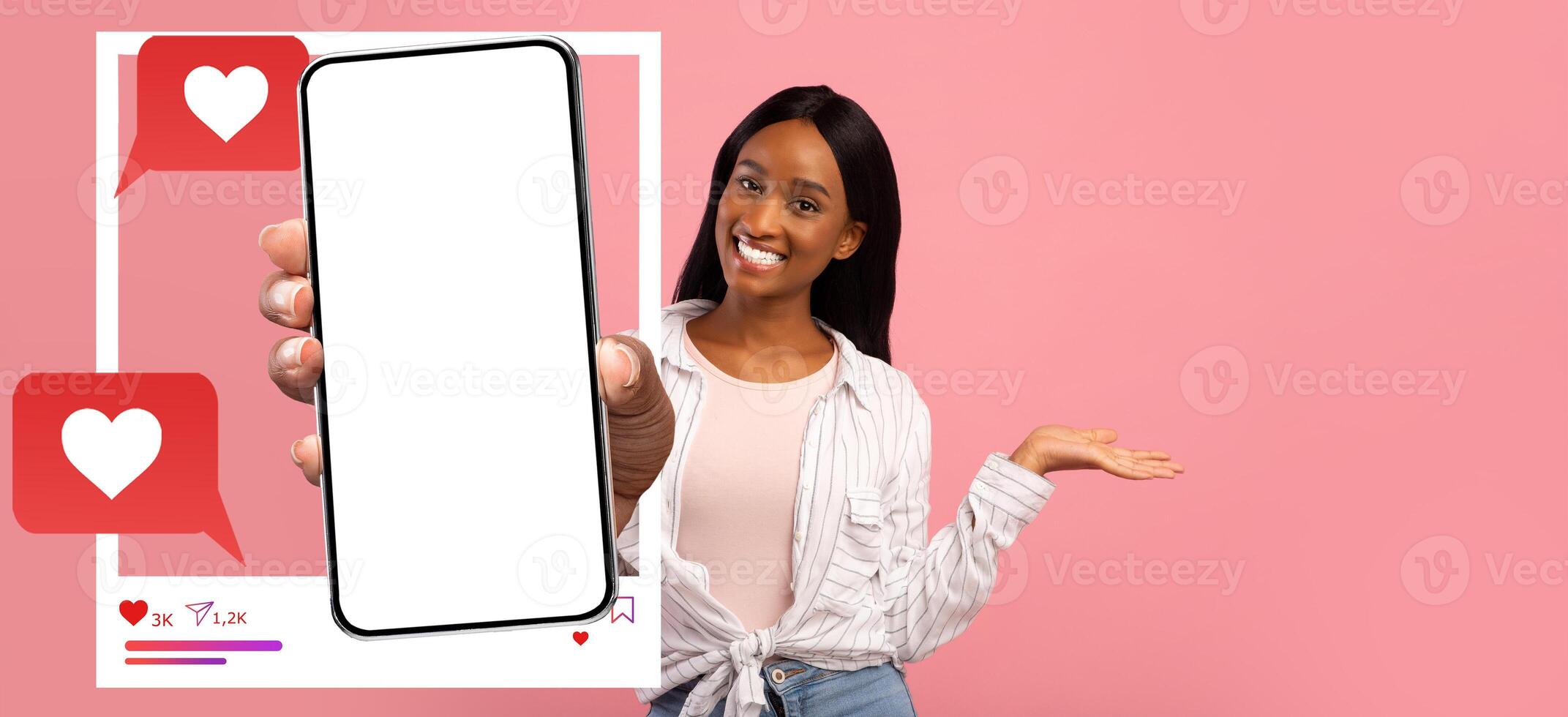 A smiling influencer holds a smartphone displaying a blank screen, surrounded by social media icons. The vibrant pink background highlights her cheerful demeanor as she engages online. photo