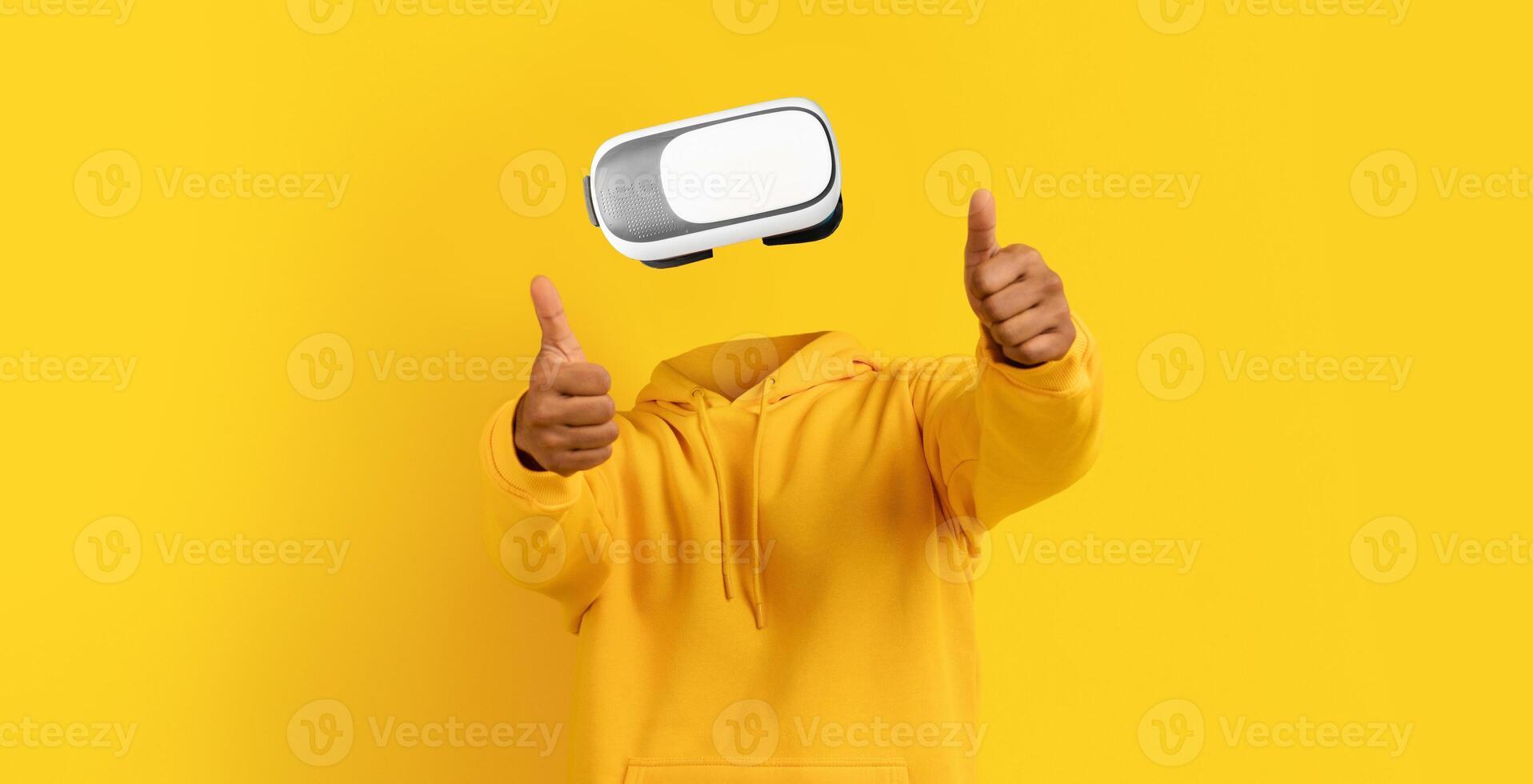 In a vibrant yellow background, a user wearing modern virtual reality goggles gives a thumbs up, showcasing excitement for the immersive experience offered by the device. photo