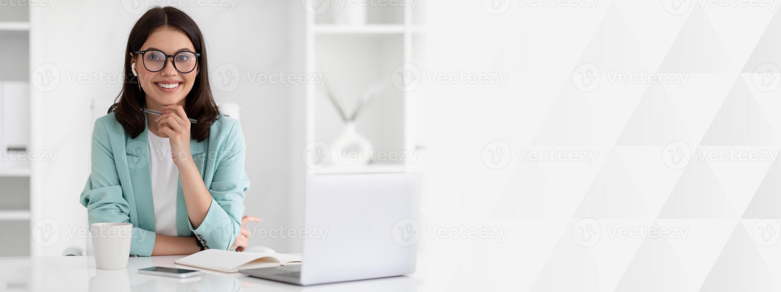 Positive millennial caucasian lady in suit and glasses at workplace with laptop, enjoy coffee in office interior. Work of manager remotely, business with device, ad and offer photo