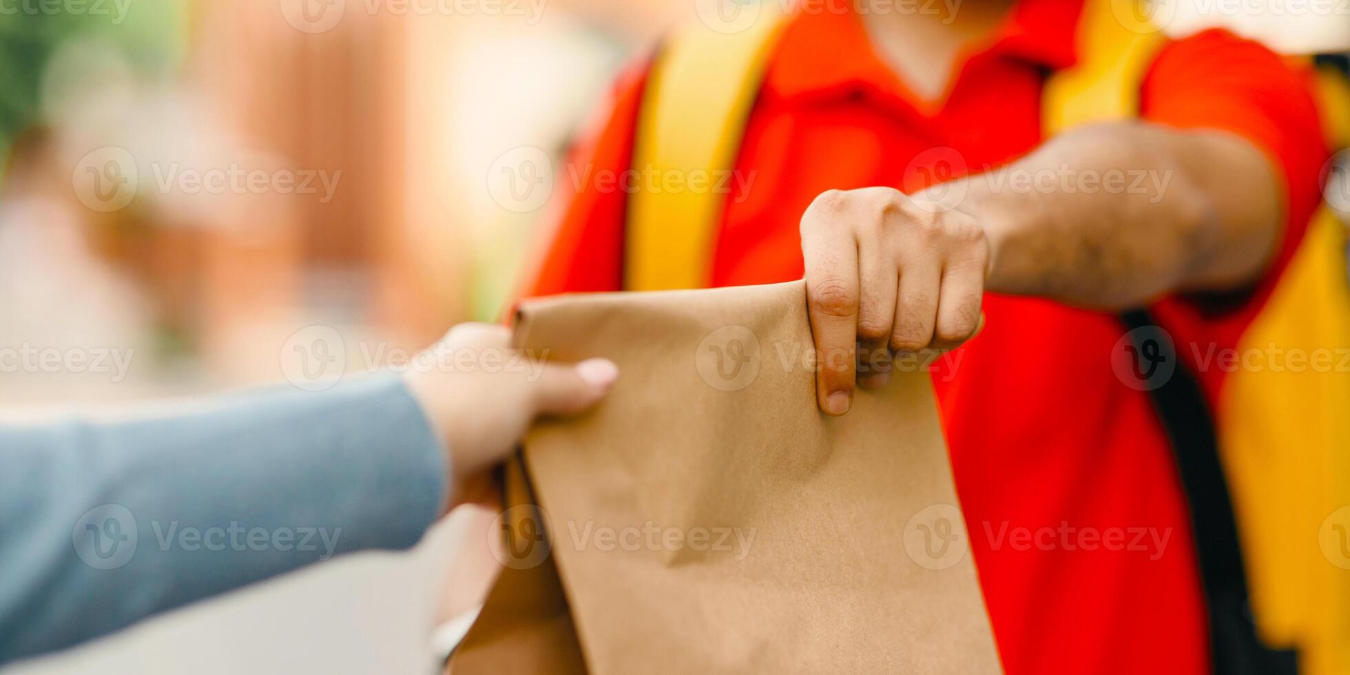 Give order to client in town. Deliveryman in uniform with yellow backpack holds paper bag, outside, cropped, close up, free space photo