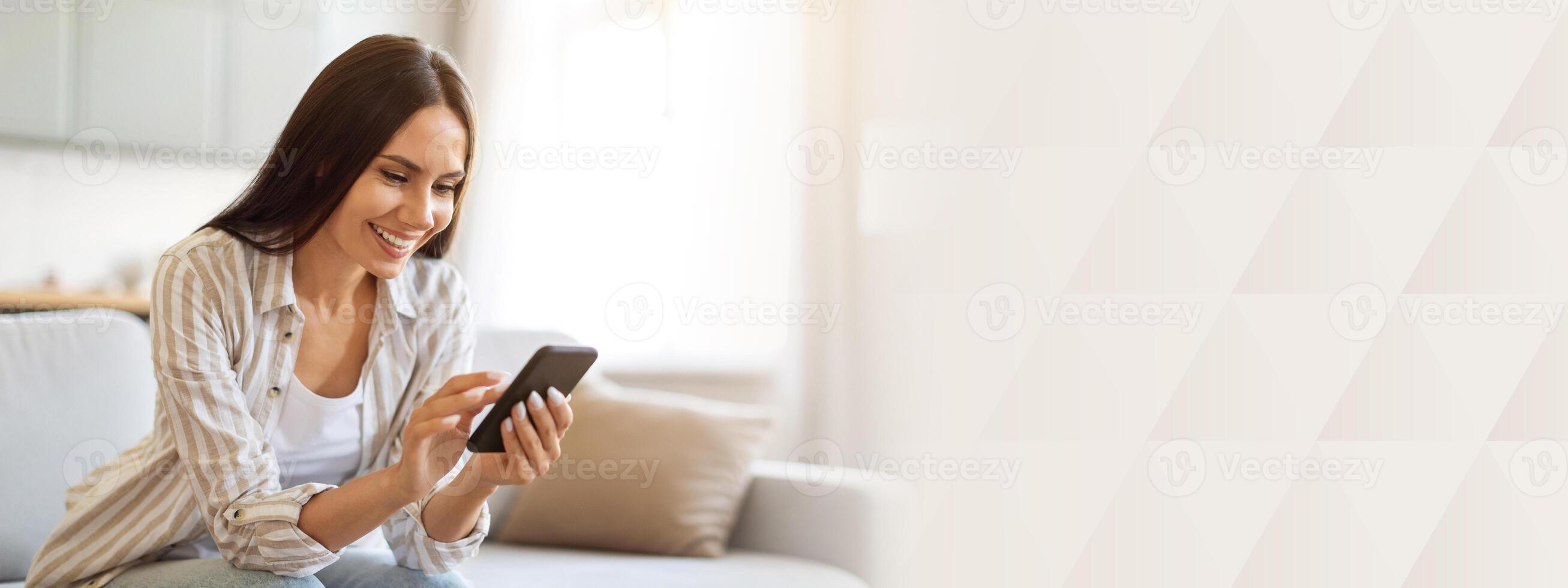 Smiling Young Woman Using Smartphone While Resting On Couch At Home, Happy Millennial Lady Sitting On Sofa And Using Mobile Phone, Shopping Online Or Browsing Social Networks, Copy Space photo