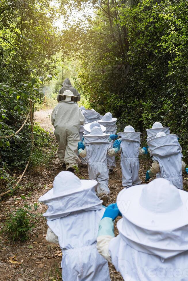 Company of kids in protective costumes in apiary photo