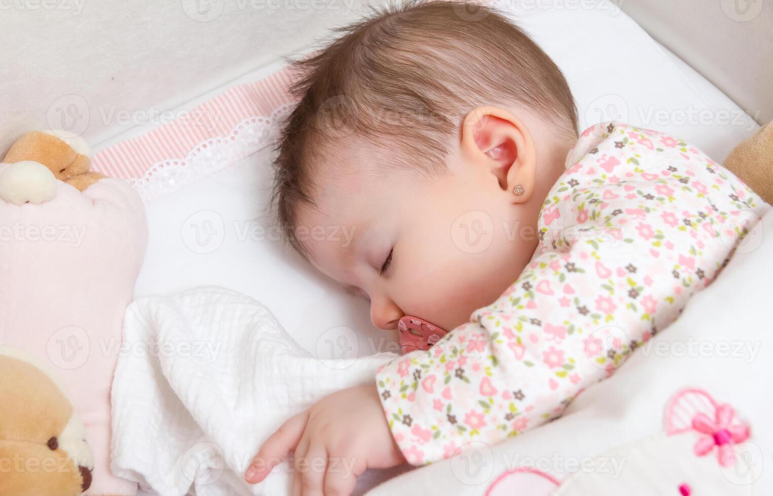 Baby girl sleeping in a cot with pacifier and toy photo