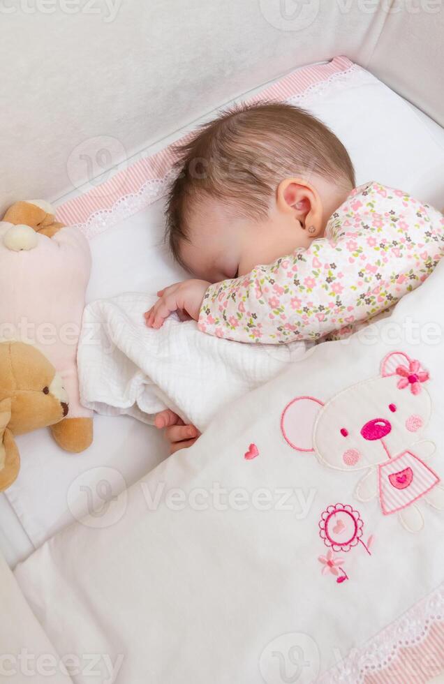 Baby girl sleeping in a cot with pacifier and toy photo