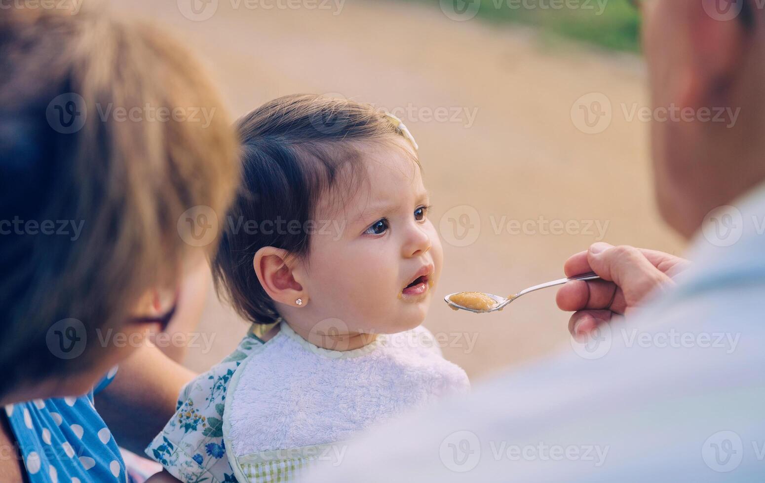 Senior man feeding to baby girl sitting in a bench photo