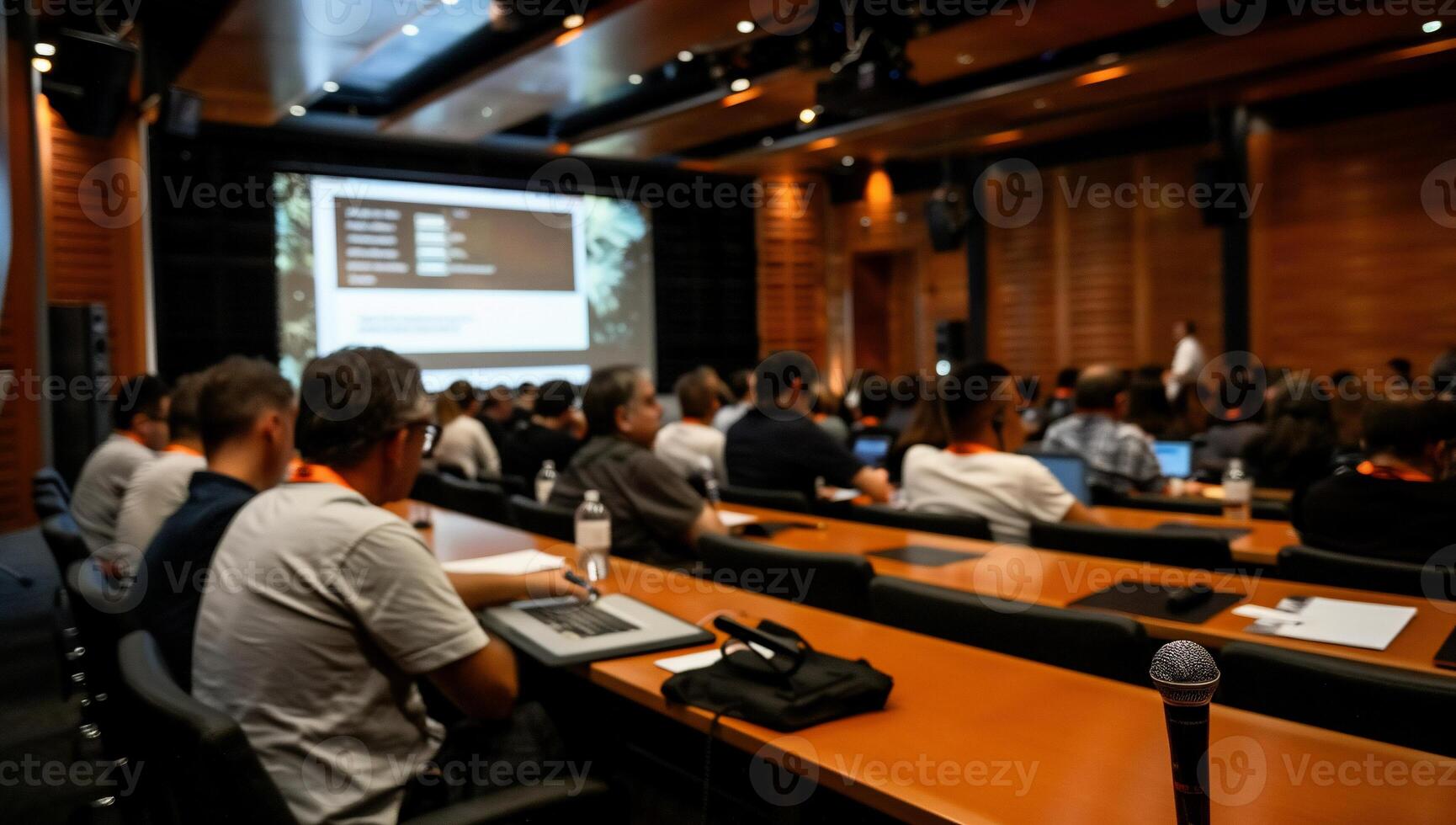 Attendees in a large conference hall, focused on a presentation photo