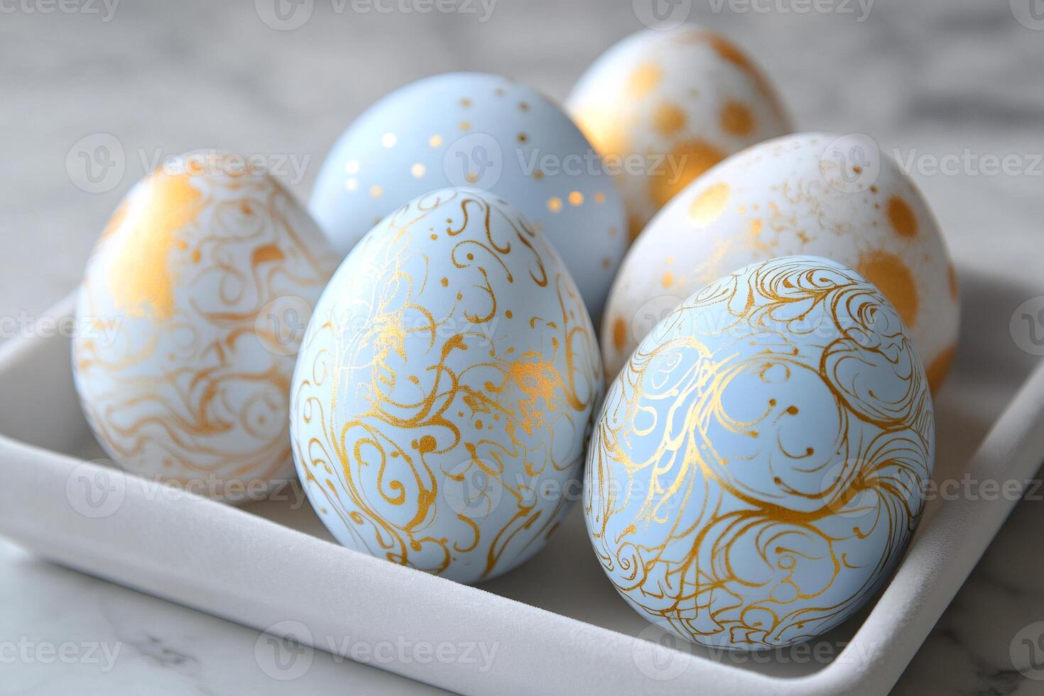 Easter eggs decorated with gold and light blue patterns lying on white ceramic tray photo
