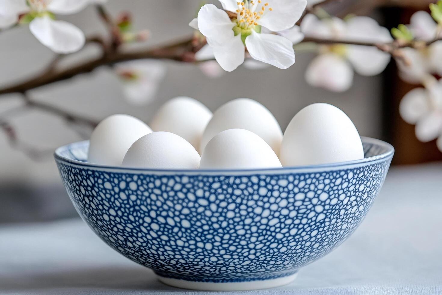 White eggs in blue bowl decorating spring table with blooming tree branch photo