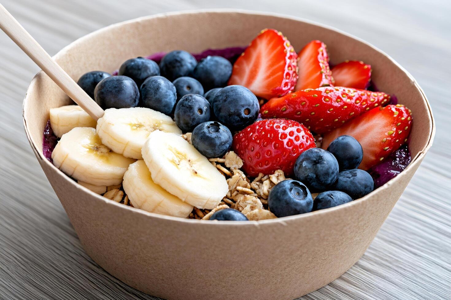 Smoothie bowl with granola, banana slices, blueberries and strawberries, containing a wooden spoon photo
