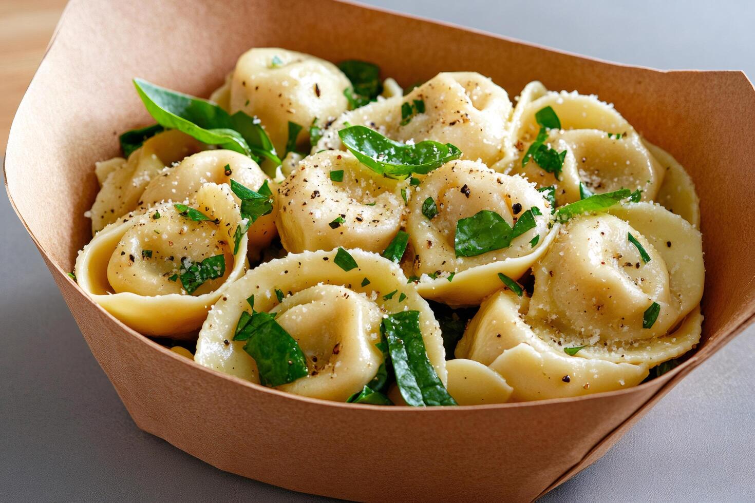 Tortellini with parmesan and basil leaves resting in a cardboard takeaway box photo