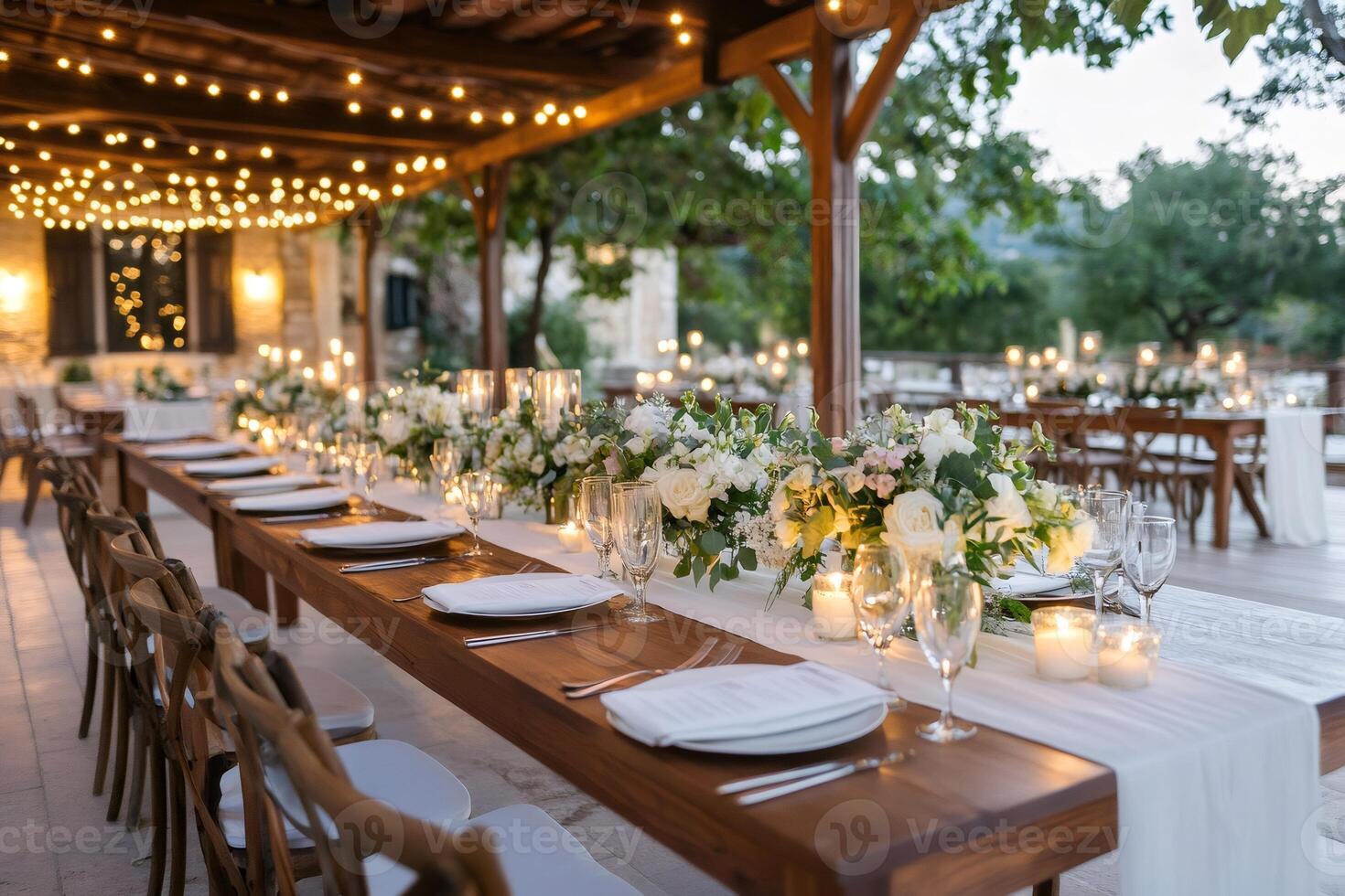 Wedding reception table is lit by candles and string lights under a wooden canopy photo