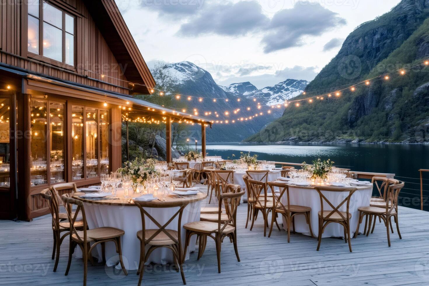 Outdoor wedding reception venue overlooking a fjord in Norway with string lights illuminating round tables photo