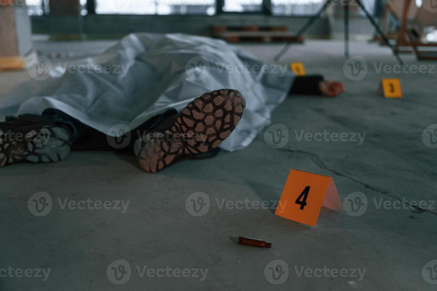Bullet shell as clue. Dead body of a man is on the ground, covered in white cloth. Conception of murder, homicide photo