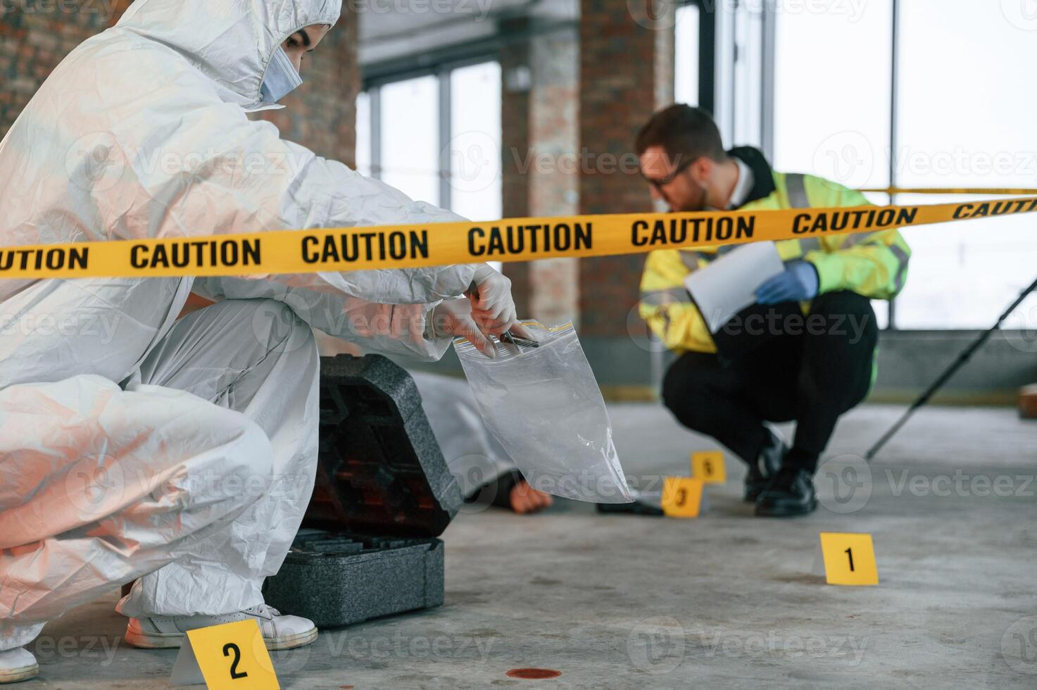 Woman, holds the sleeve from the cartridge and puts it in the bag. Detectives are collecting evidence in a crime scene near dead body photo