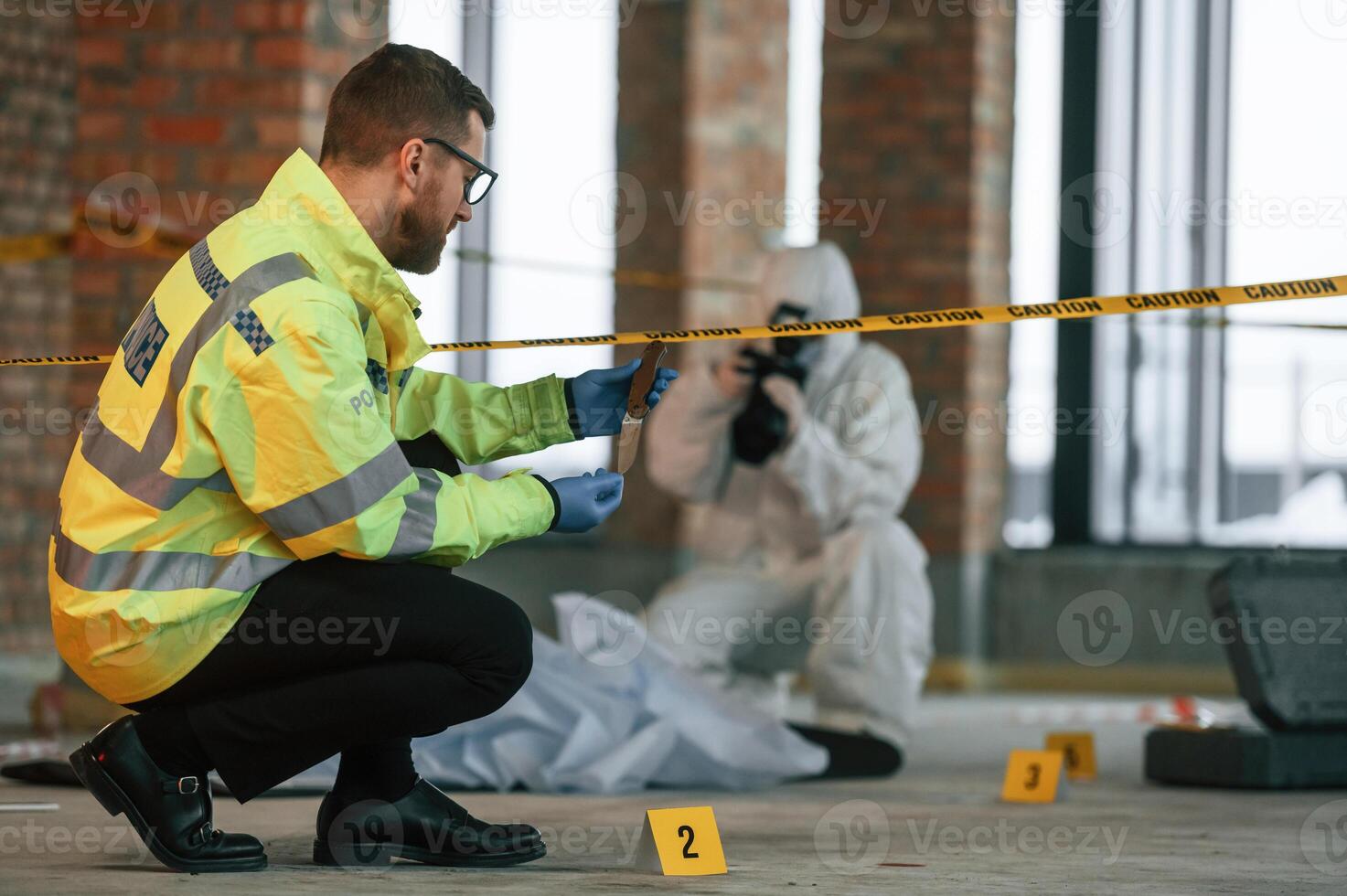 Woman is using camera,, making photos. Detectives are collecting evidence in a crime scene near dead body photo