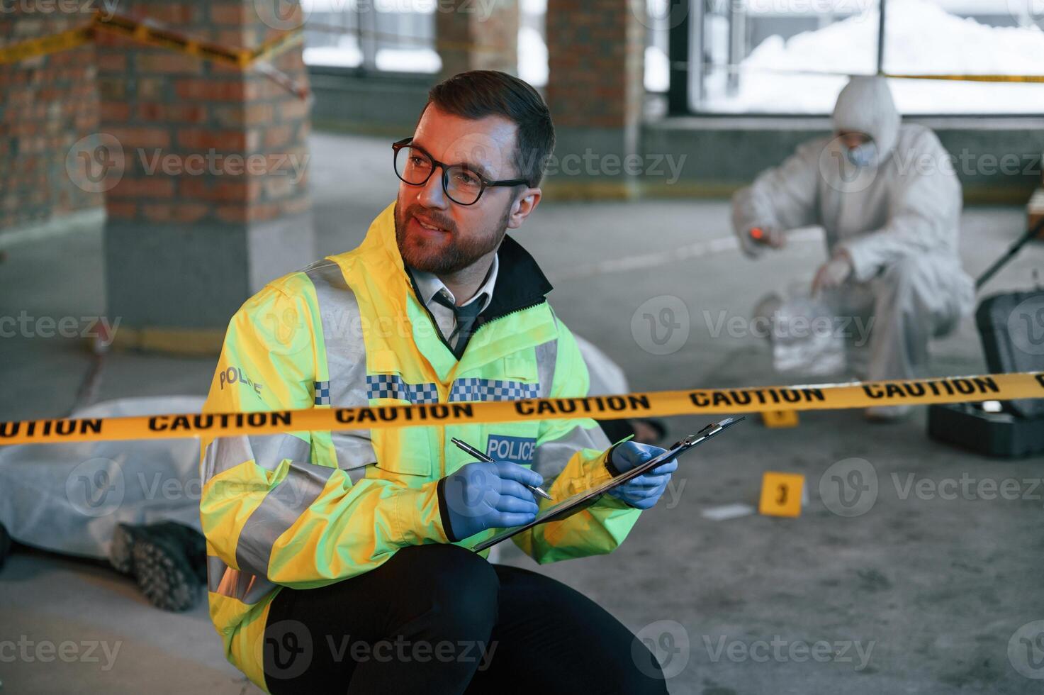 Sitting, near caution police tape. Detectives are collecting evidence in a crime scene with dead body photo