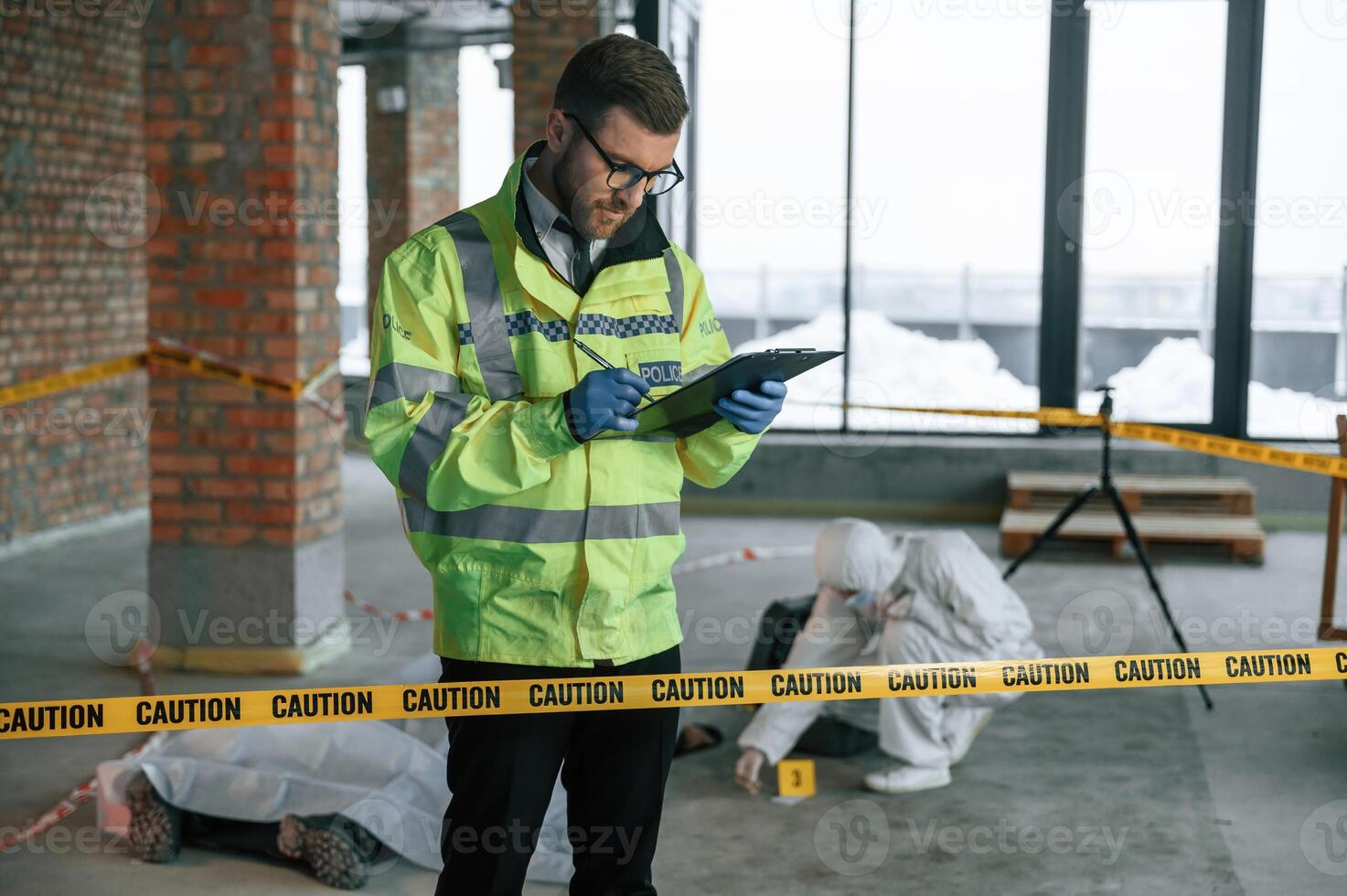 Man, writing information into notepad. Detectives are collecting evidence in a crime scene near dead body photo
