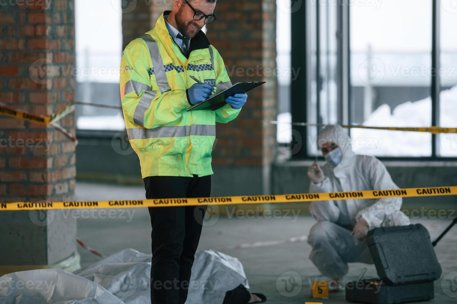 Man is standing and smiling. Detectives are collecting evidence in a crime scene near dead body photo