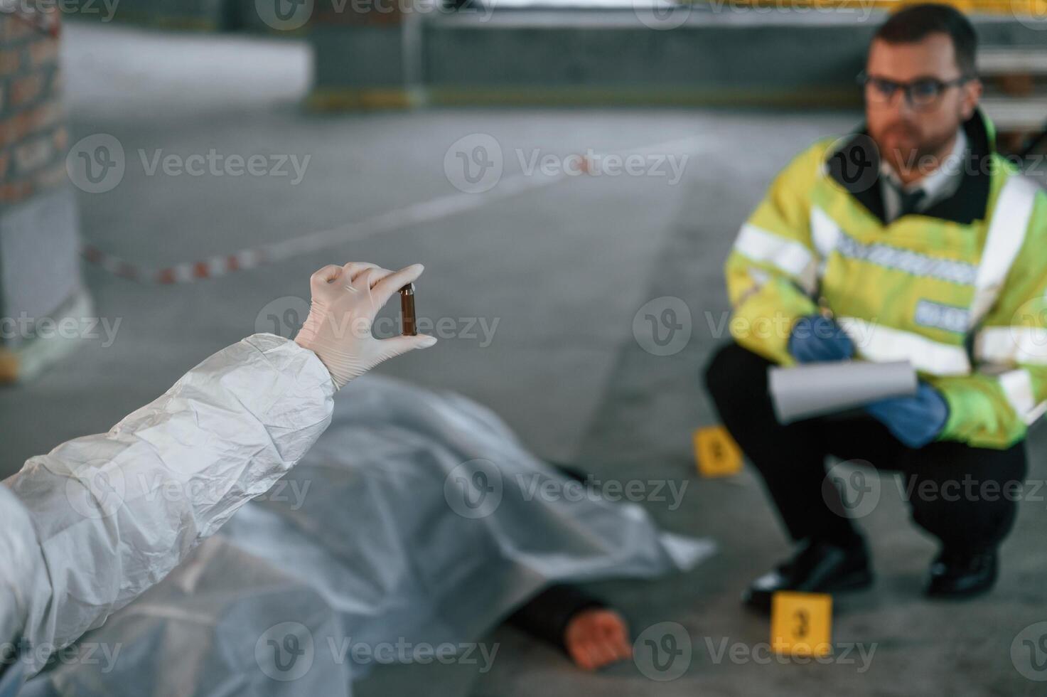 A woman is holding a shell casing. Detectives are collecting evidence in a crime scene near dead body photo