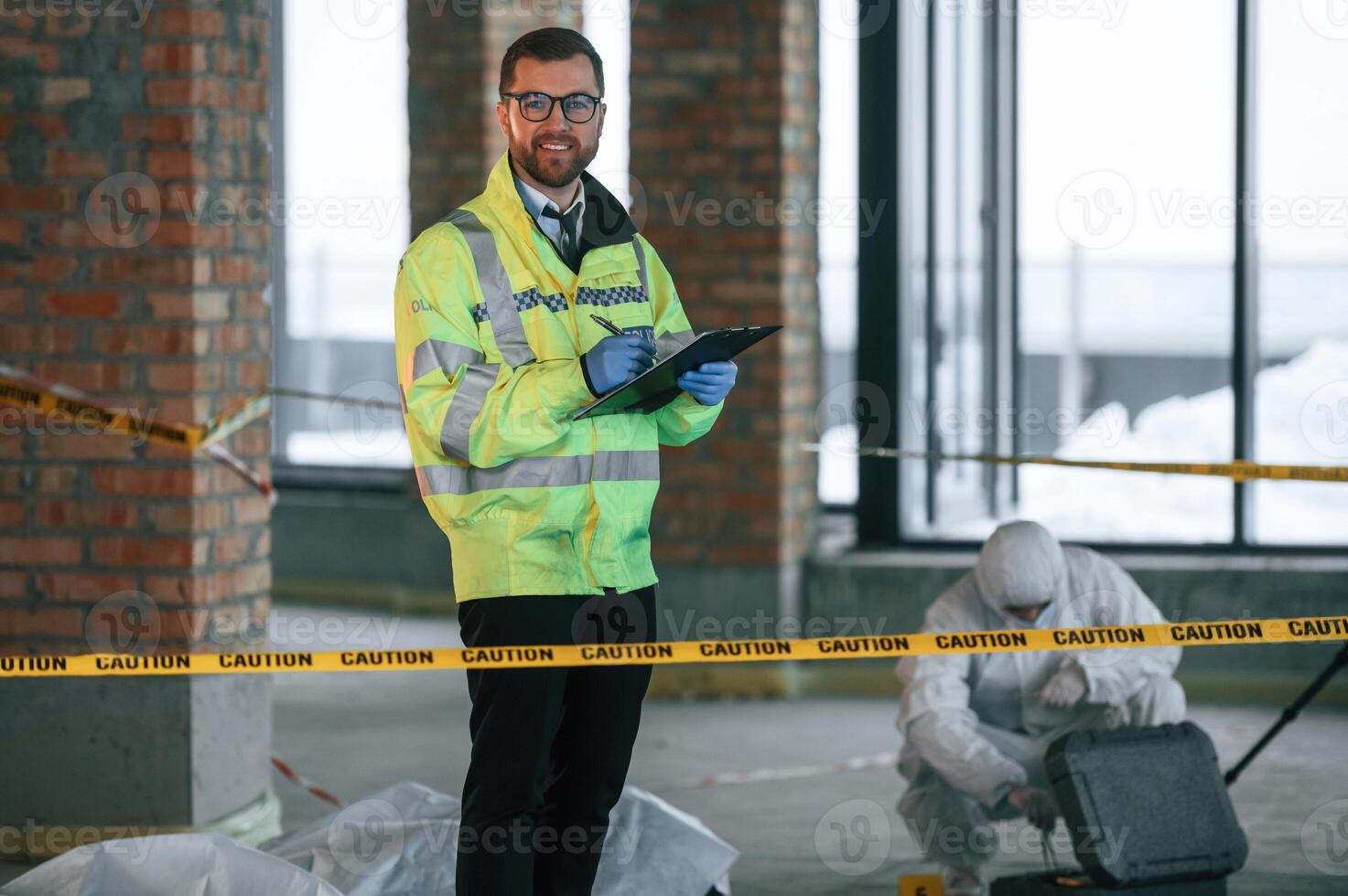 Man is, standing and smiling. Detectives are collecting evidence in a crime scene near dead body photo