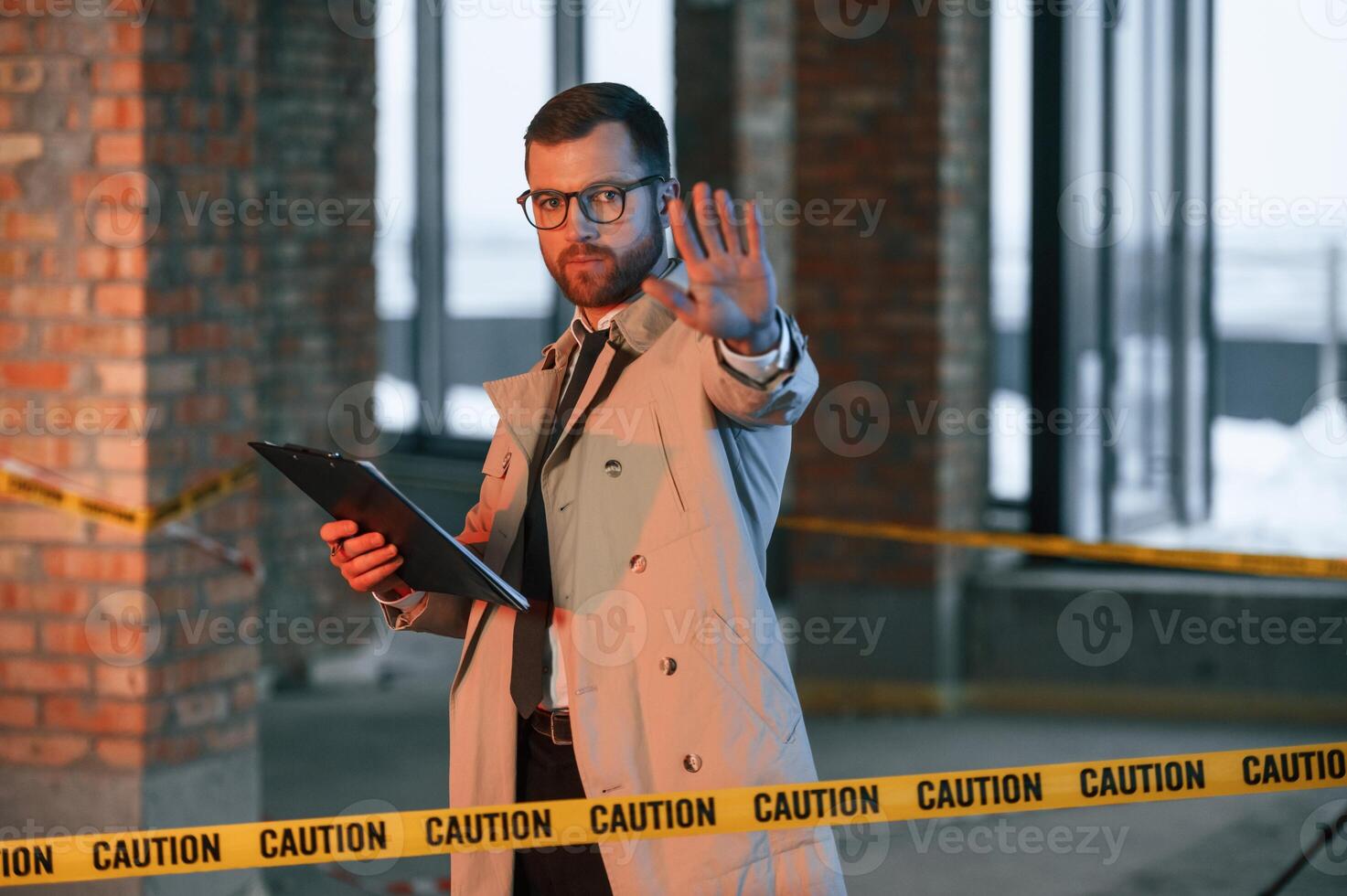 Stop gesture.. No trespassing.. Male detective in coat is collecting evidence in a crime scene on the construction site photo