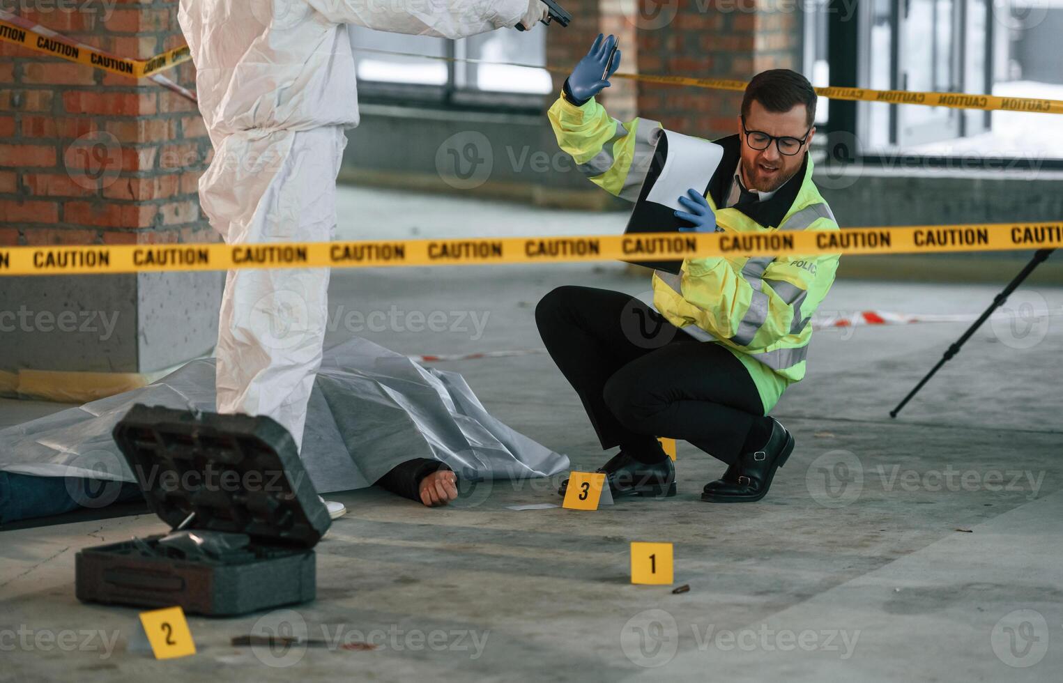 Police worker is sitting on the ground near the dead body while woman is standing with a pistol and threatens him photo