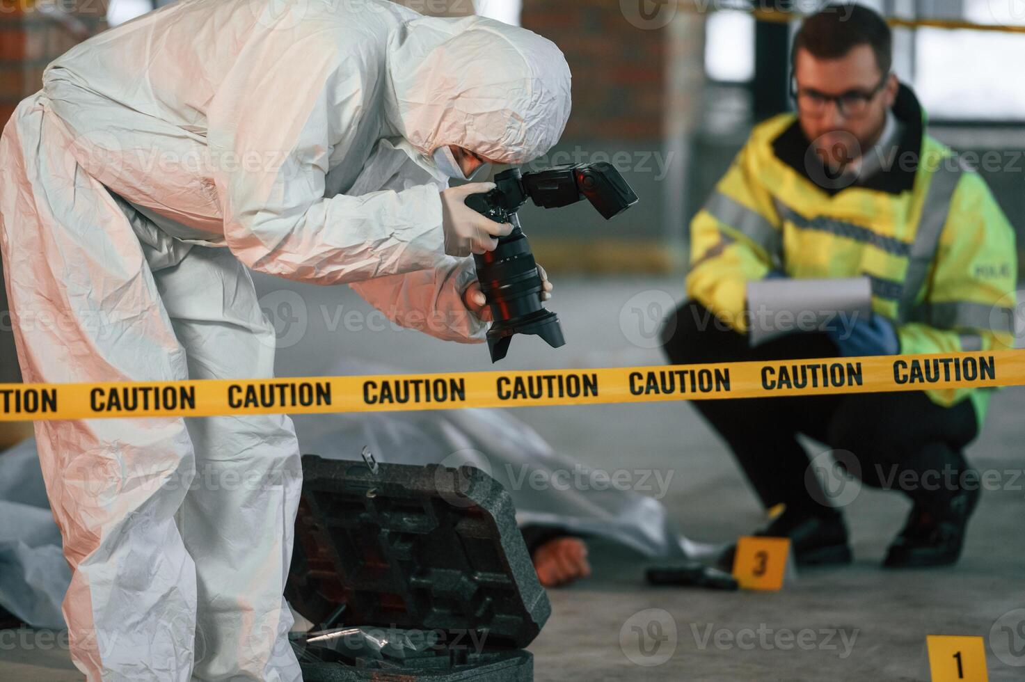 Woman is making photos by ,camera. Detectives are collecting evidence in a crime scene near dead body