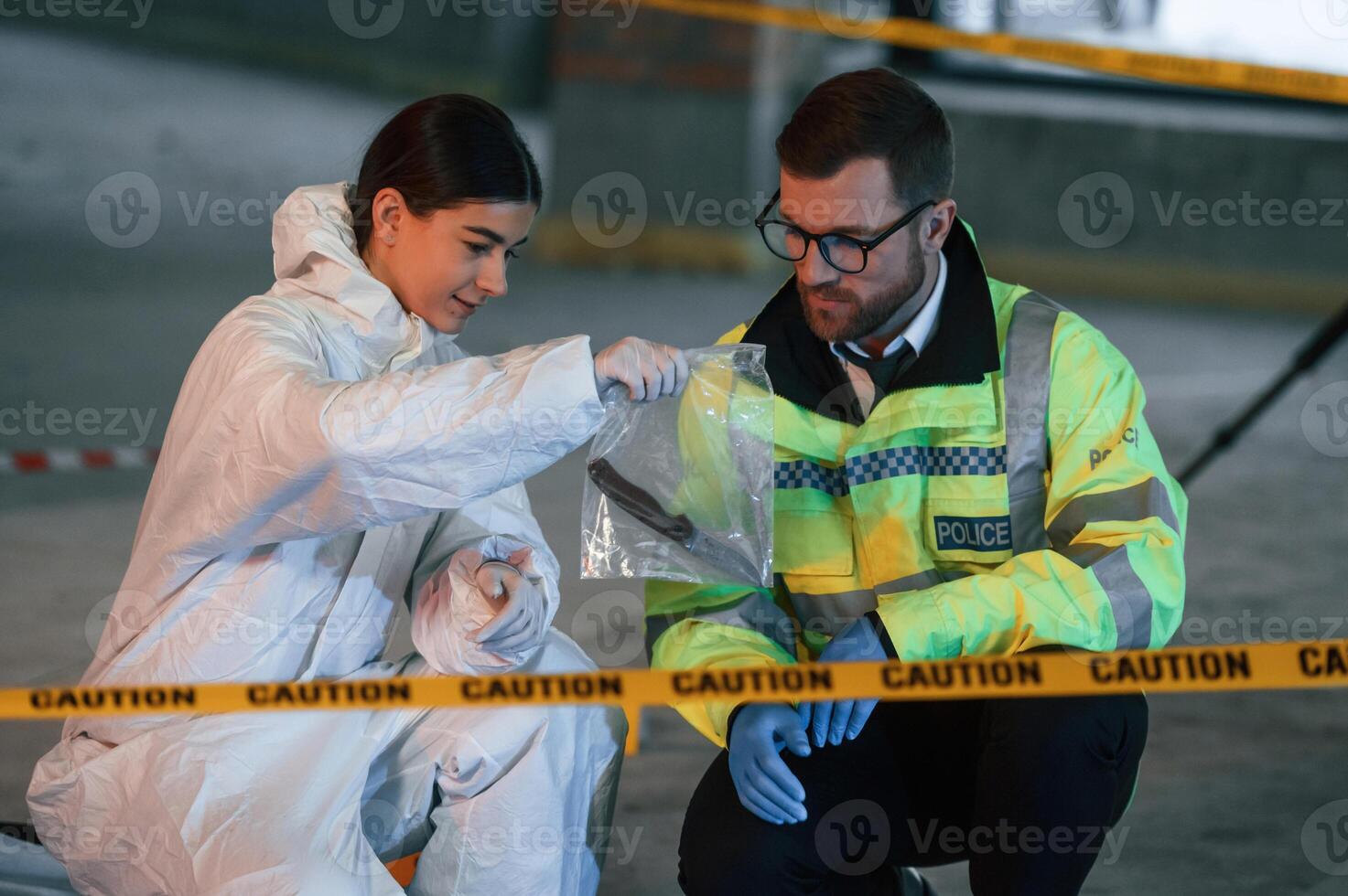 Holding ,knife in package. Two detectives are collecting evidence in a crime scene photo