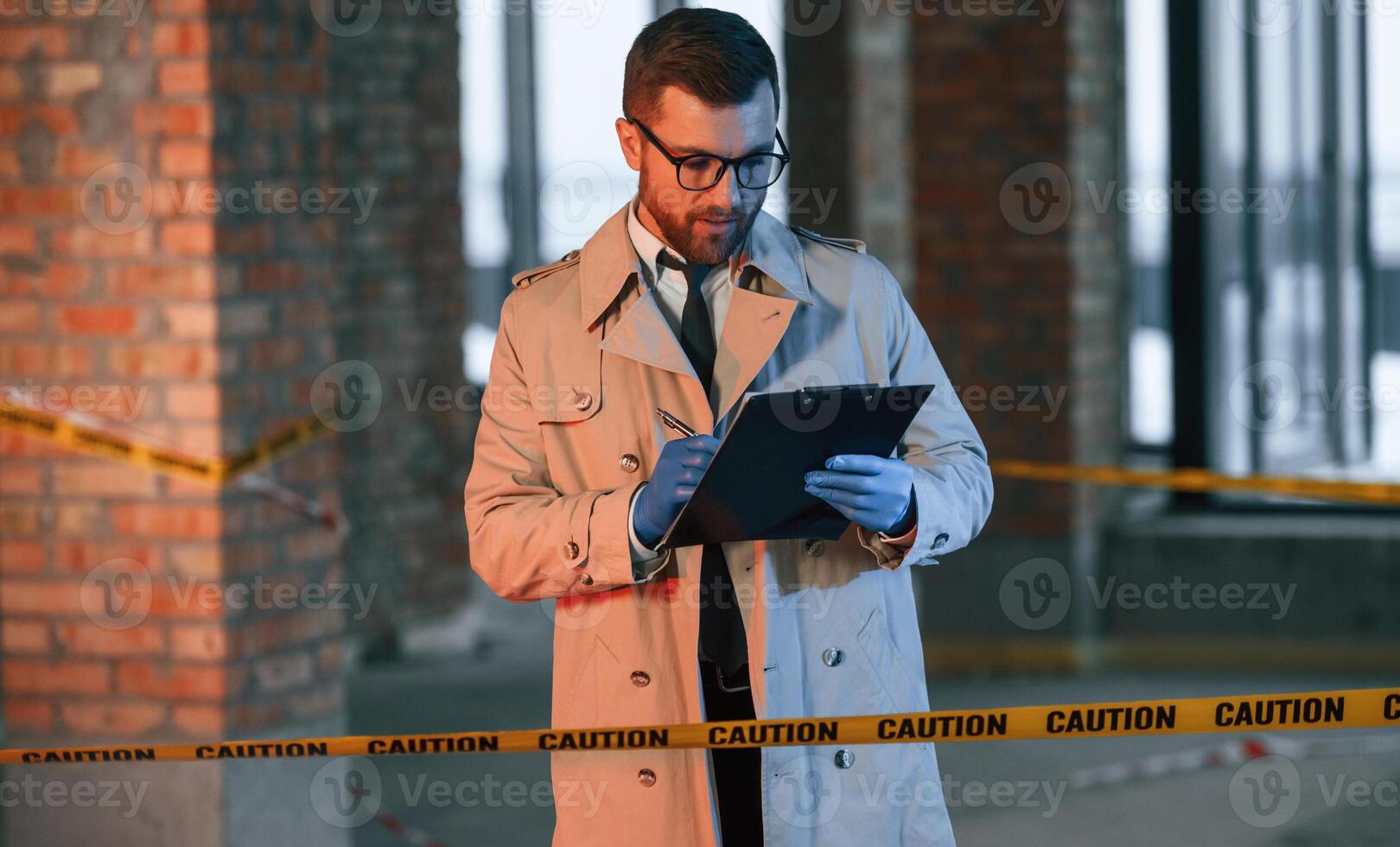 Male detective in coat is collecting evidence in a crime, scene on the construction site. With notepad in hands photo